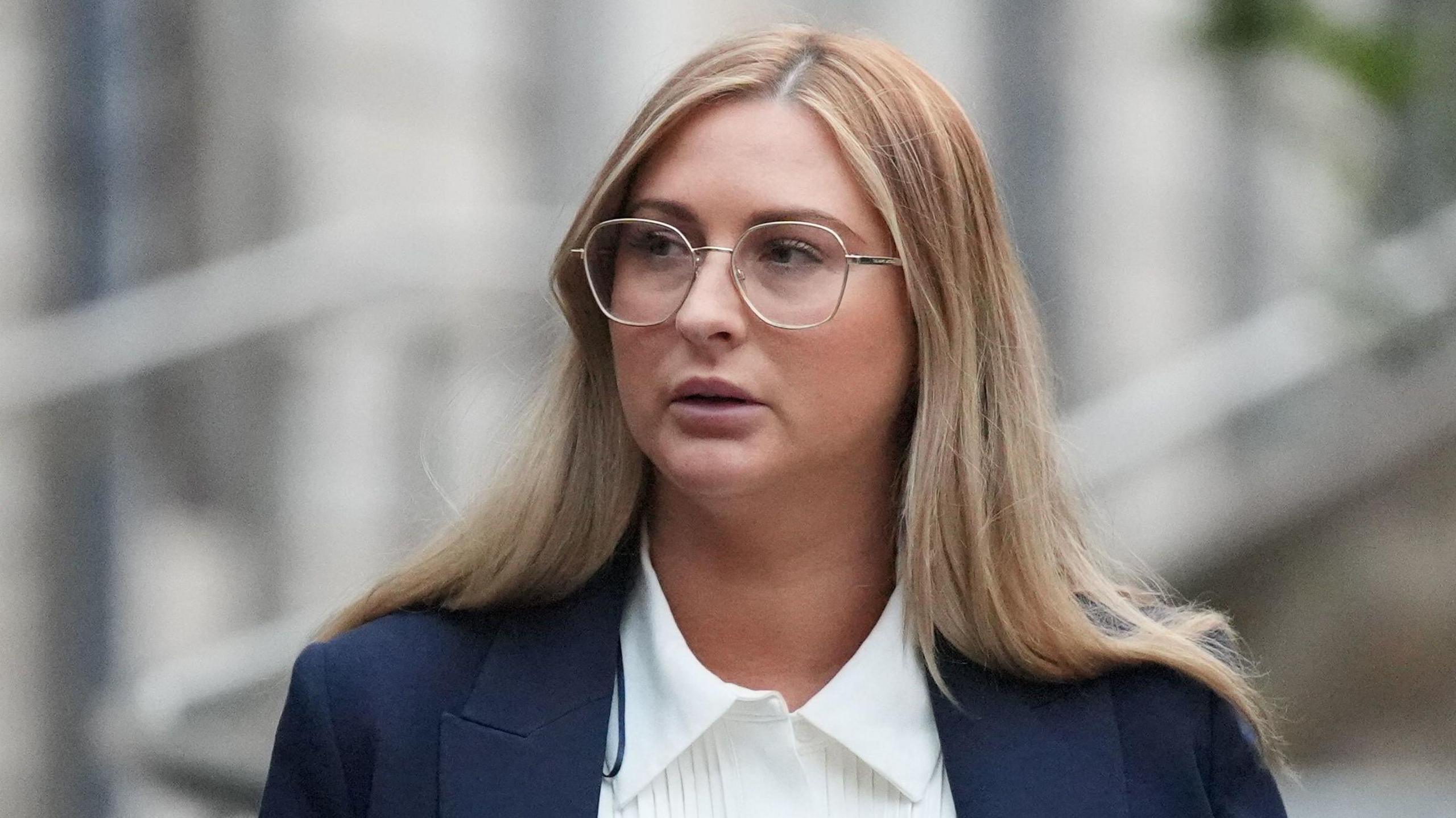 Nikita Hand outside court at an earlier appearance in the case last week.  She has long, straight, blonde hair and is wearing wide-rimmed glasses, a navy jacket and a white blouse.