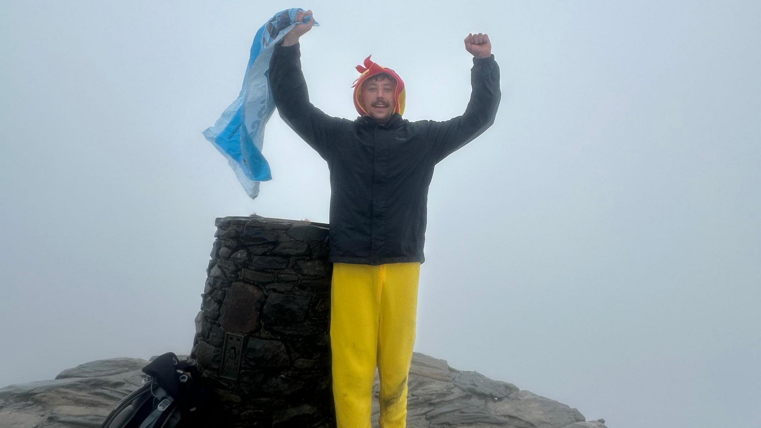 Luke next to a cairn with his arms aloft, celebrating after another climb.