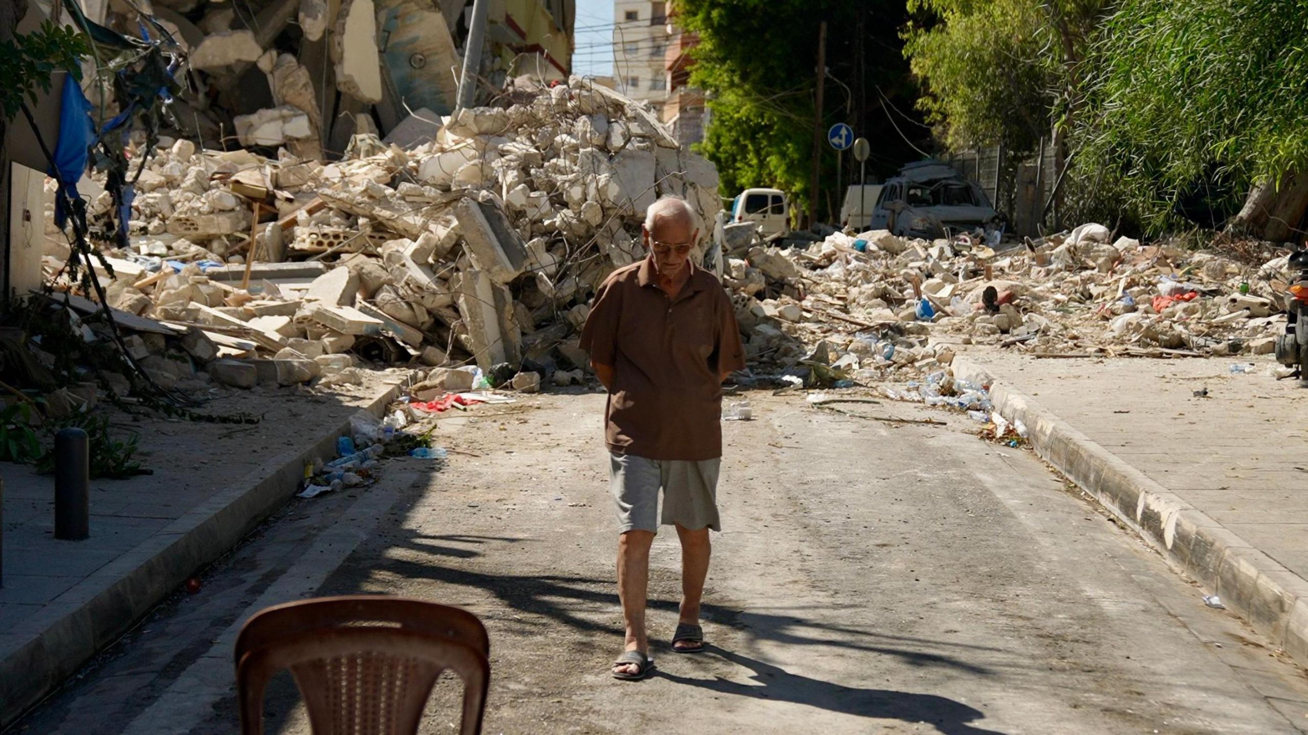 An elderly Lebanese man walks in a street surrounded by toppled buildings and rubble after Israeli air strike