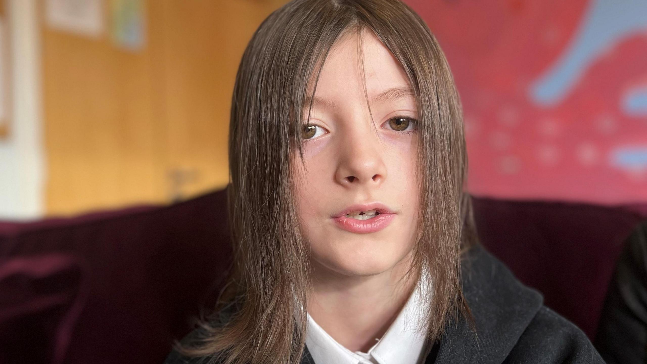 Hannah has shoulder-length dark hair and is wearing a white school shirt without a tie and black hoodie. She is looking directly at the camera