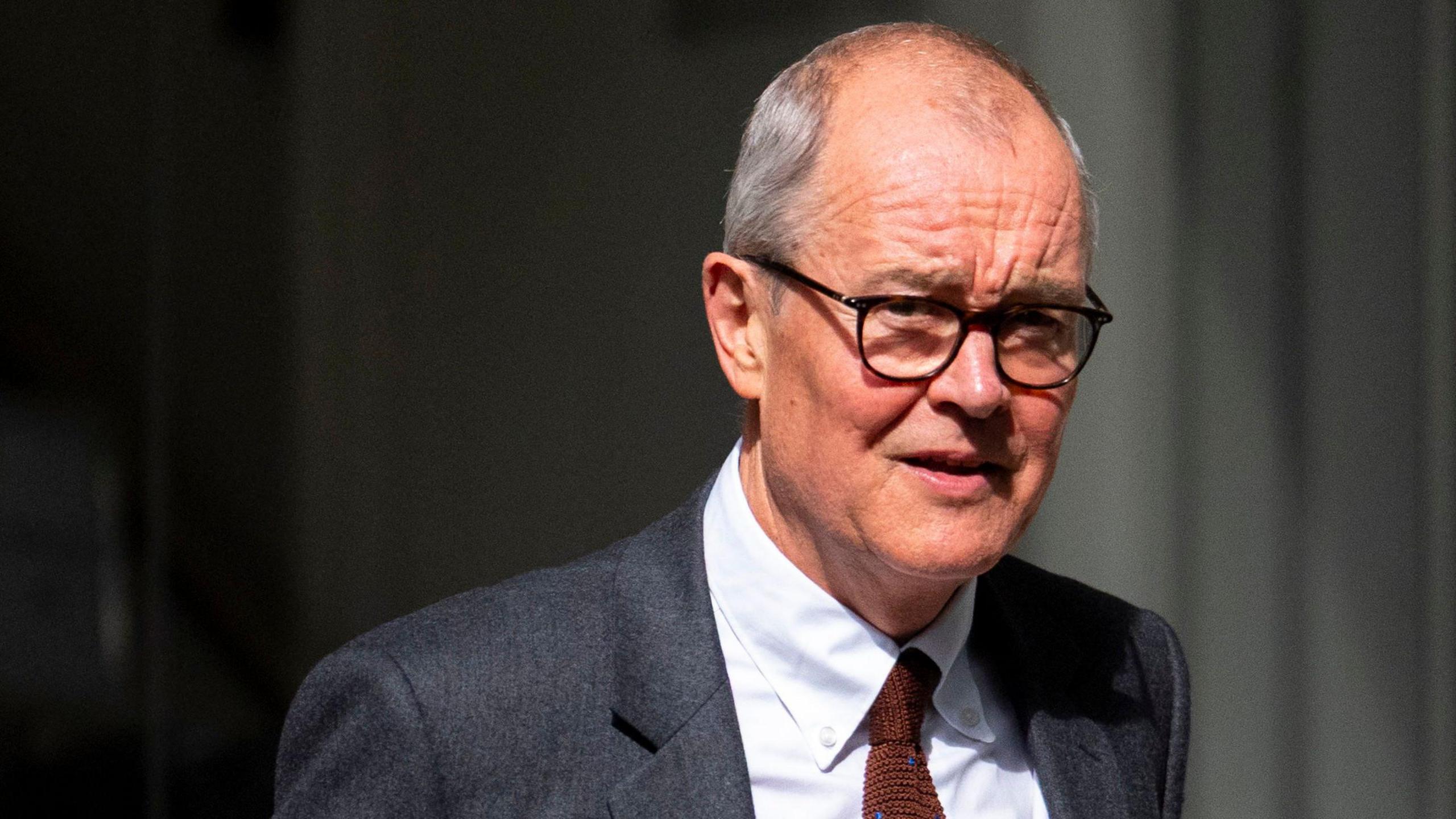 Lord Patrick Vallance has short grey hair and brown-framed glasses. He is wearing a red tie, grey blazer and white shirt.