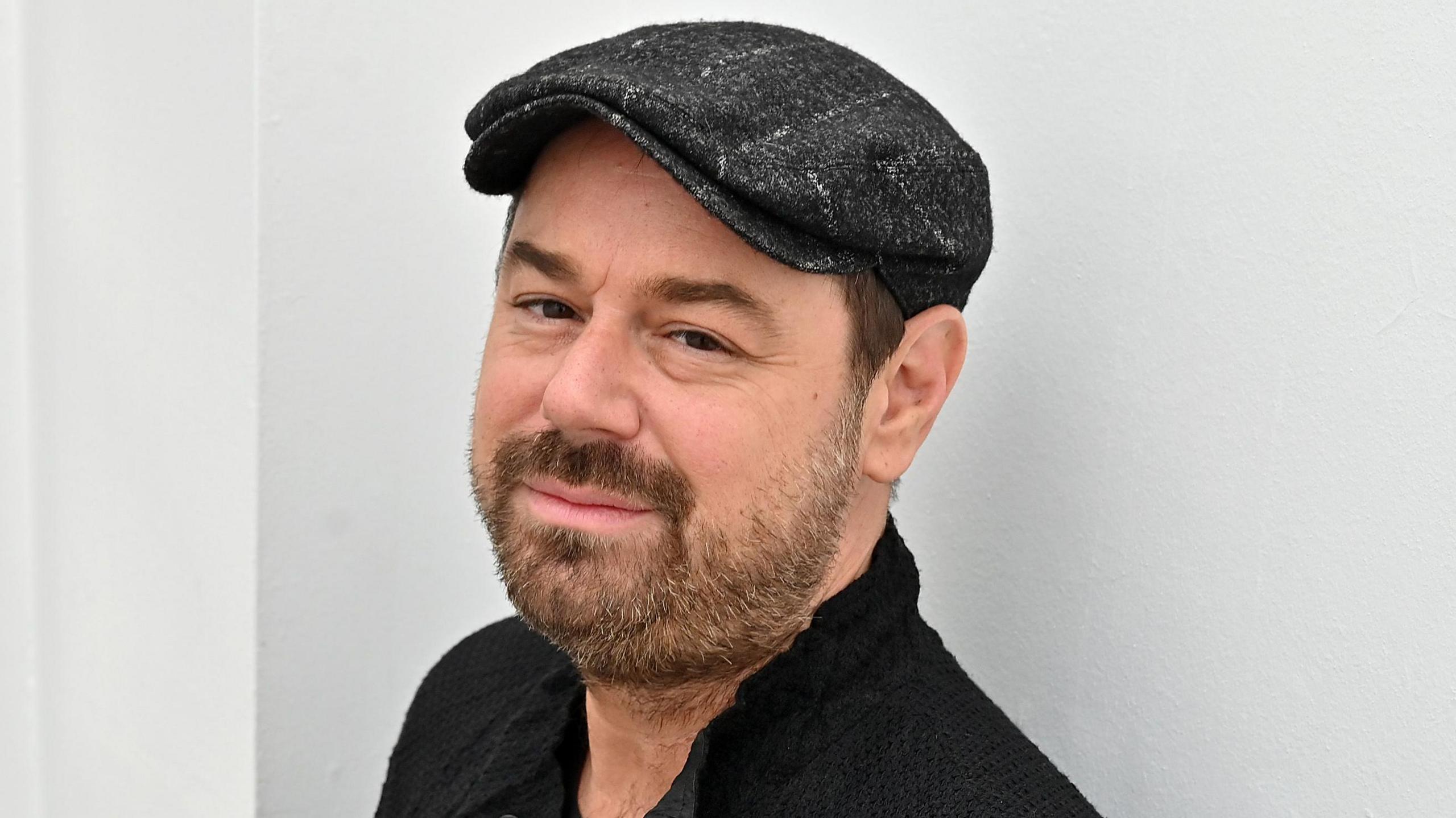 Danny Dyer wearing a black cap and smiling at the camera 