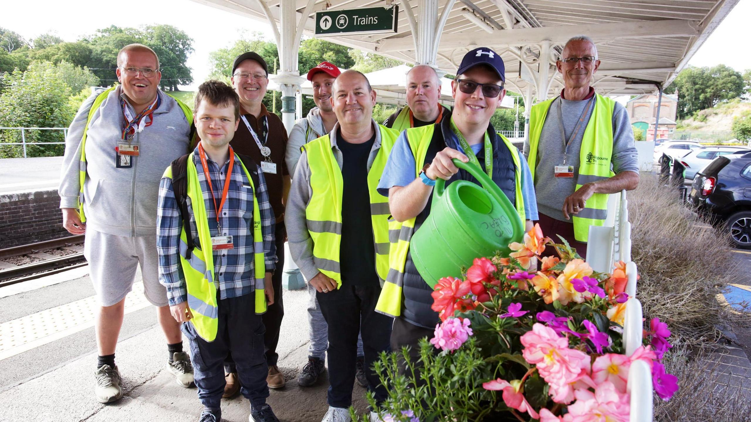 Members of The Aldingbourne Trust water a plant at a railway station