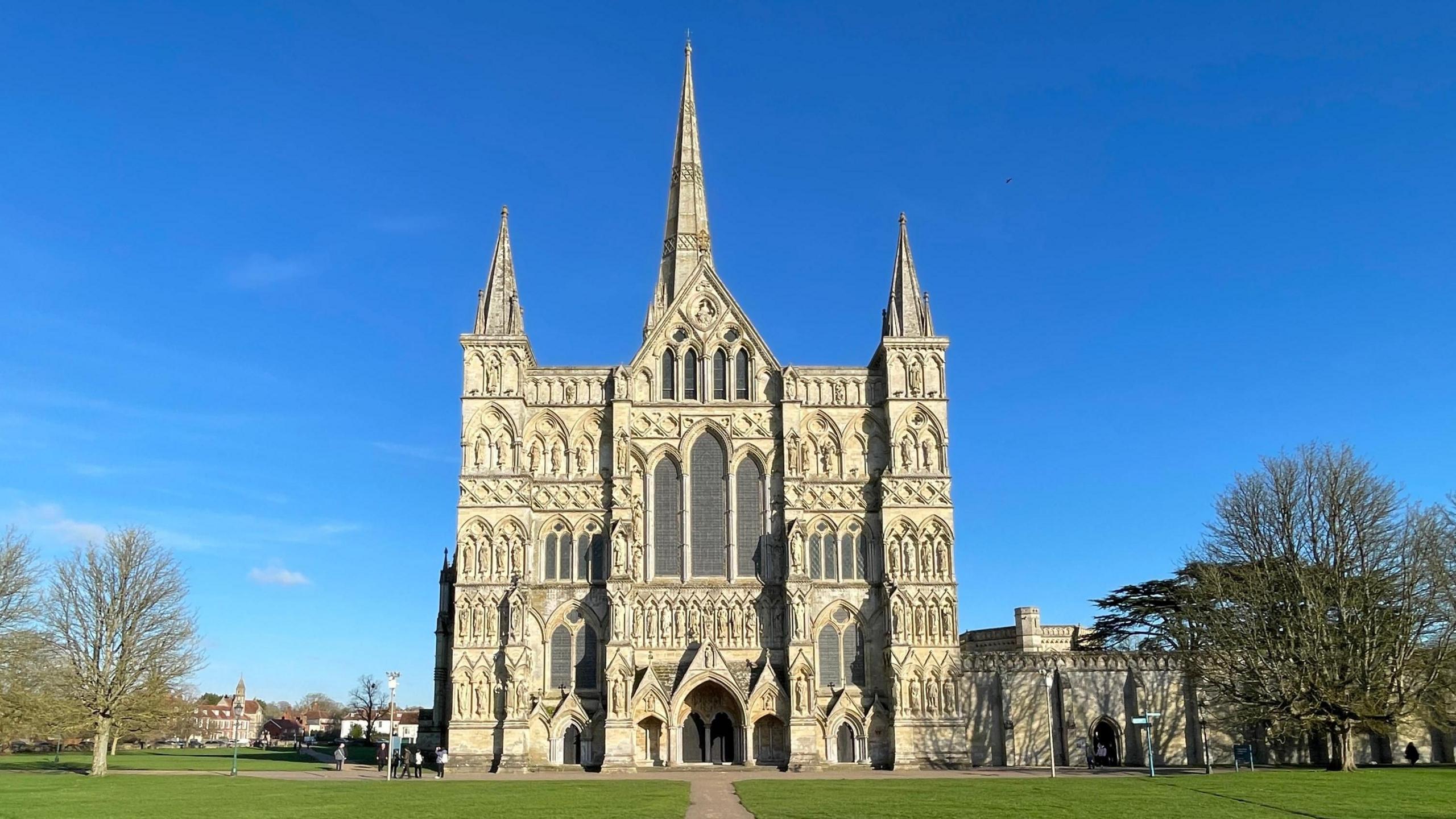 The facade of Salisbury Cathedral as seen on a sunny day with perfect blue skies behind it.
