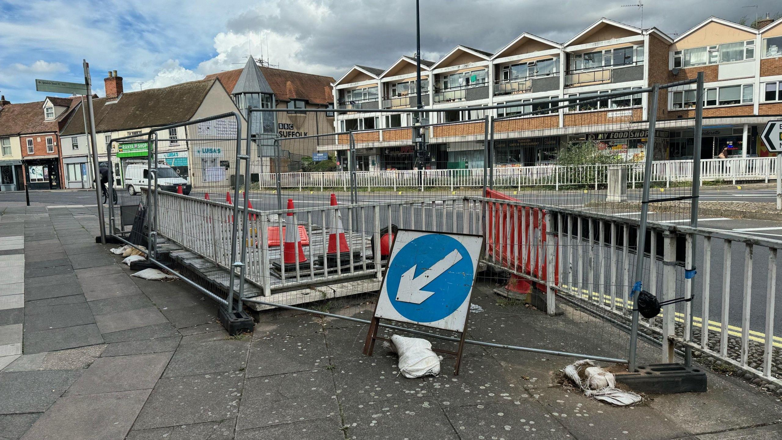 Metal barriers surround the entrance of the underpass while buildings and shops can be seen in the background.