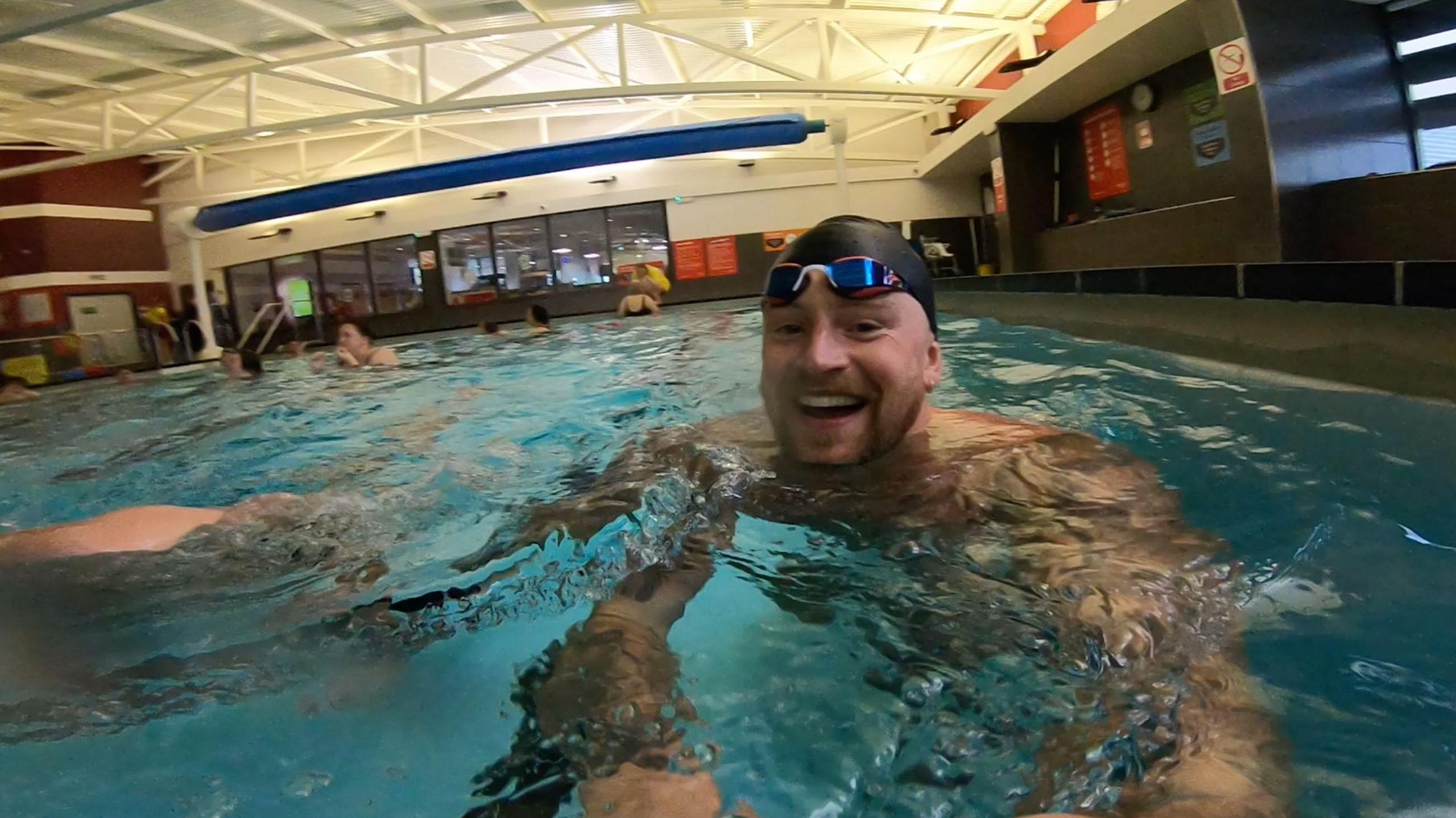 Olympic gold swimmer Adam Peaty holding a camera in the pool at Uttoxeter Leisure Centre.