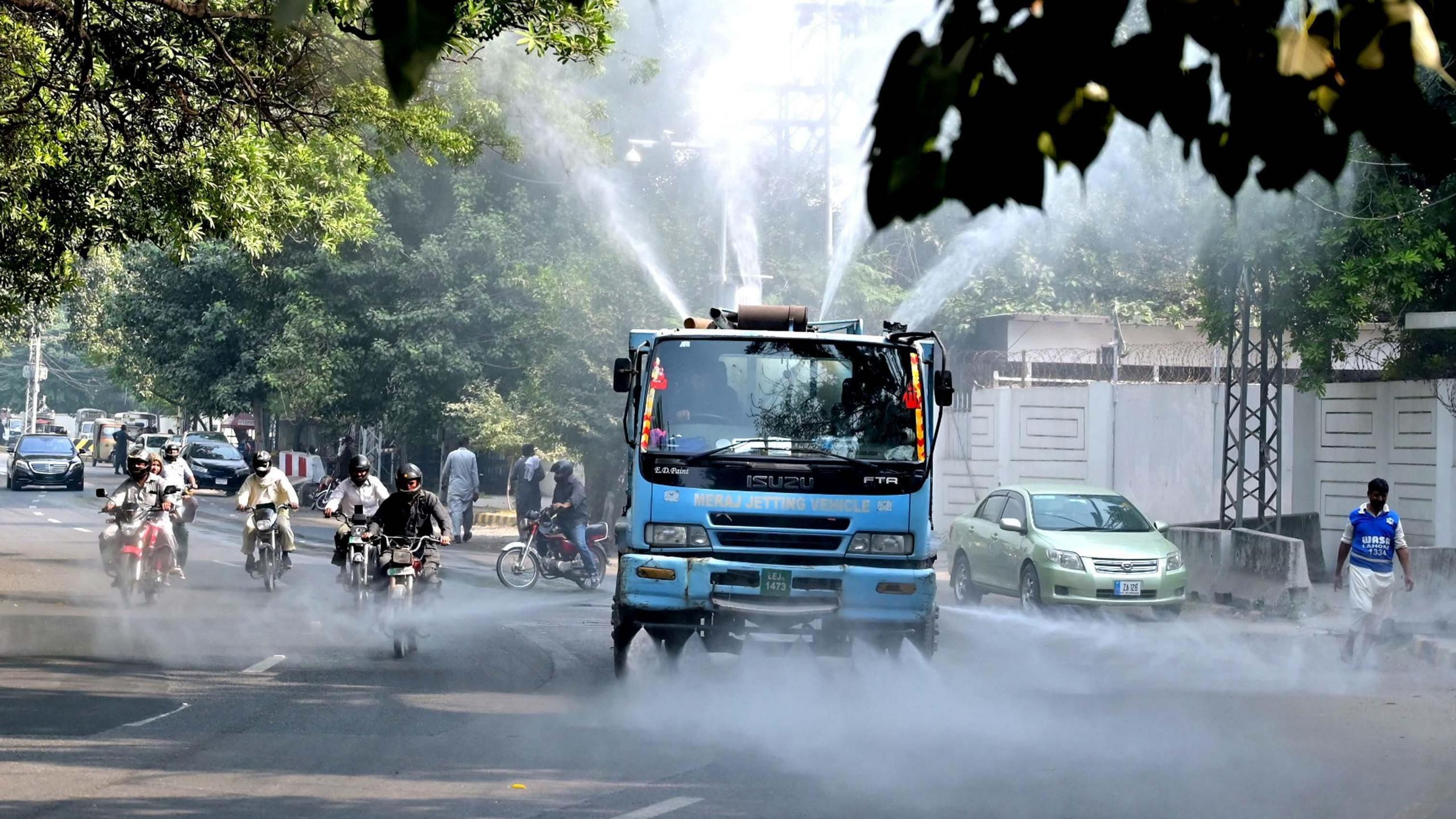 A blue vehicle sprays water into the air in Lahore as intense smog grips the city.