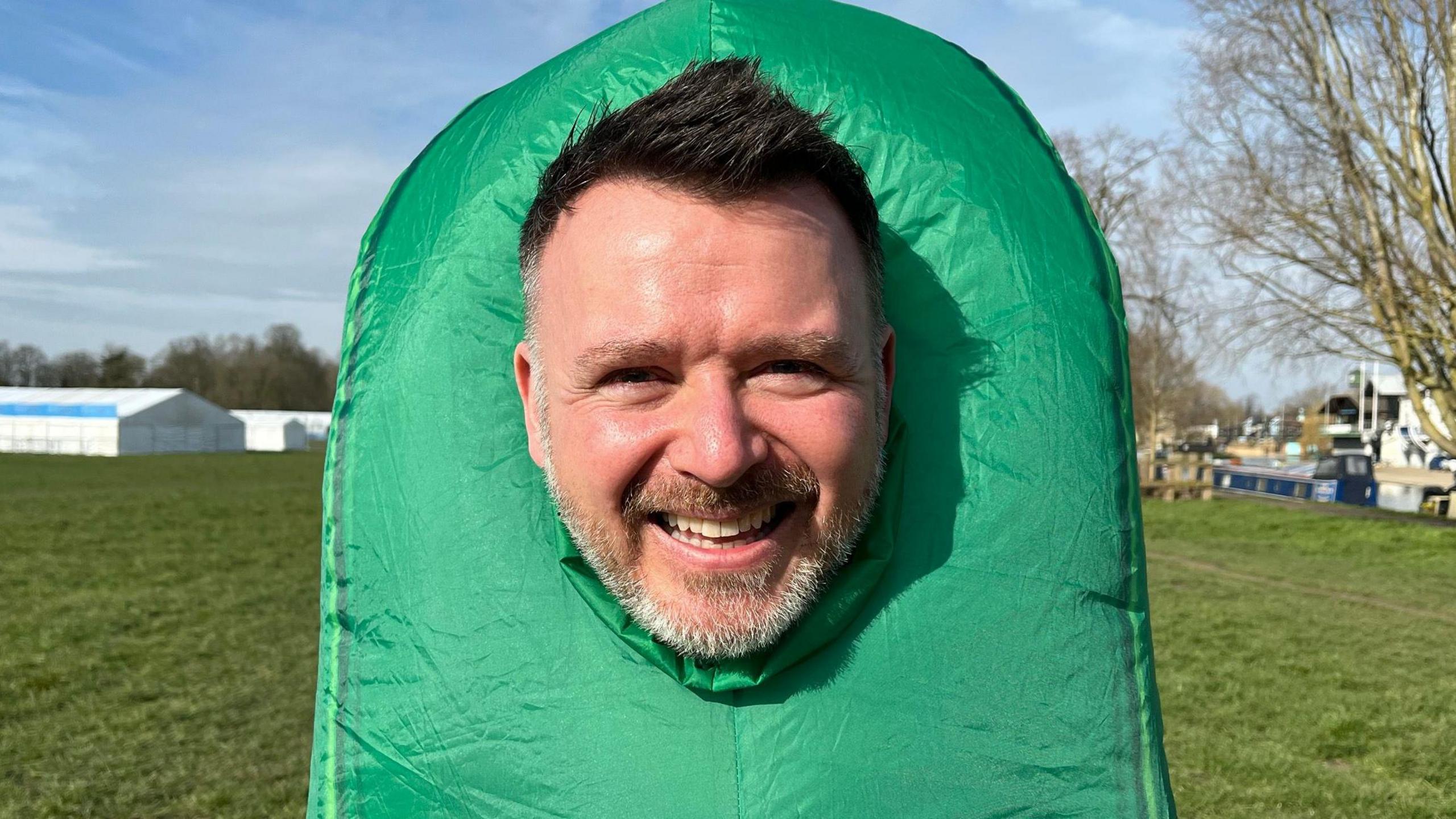 Dan Ferrandino in a green outfit dressed as a cucumber. He has short dark hair and a grey beard.