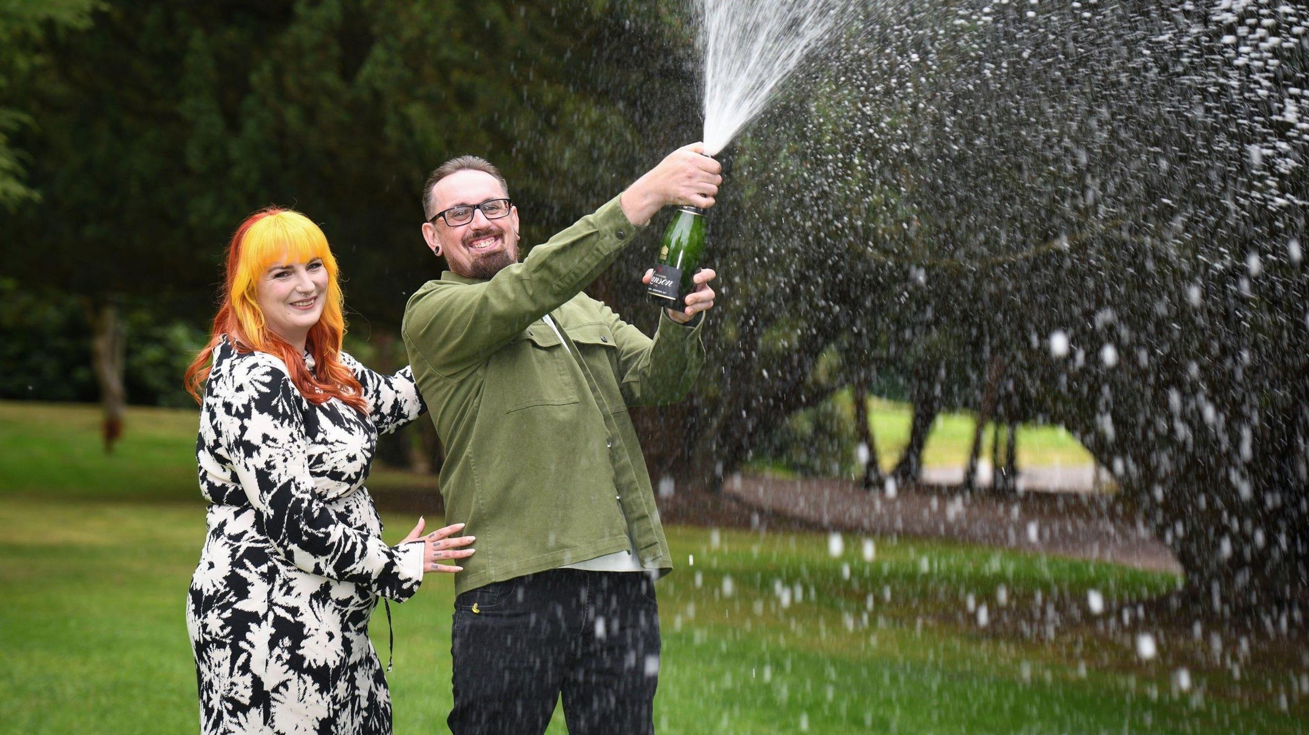 Dan and Kayleigh Cater stand together, smiling, as Dan sprays champagne from a bottle