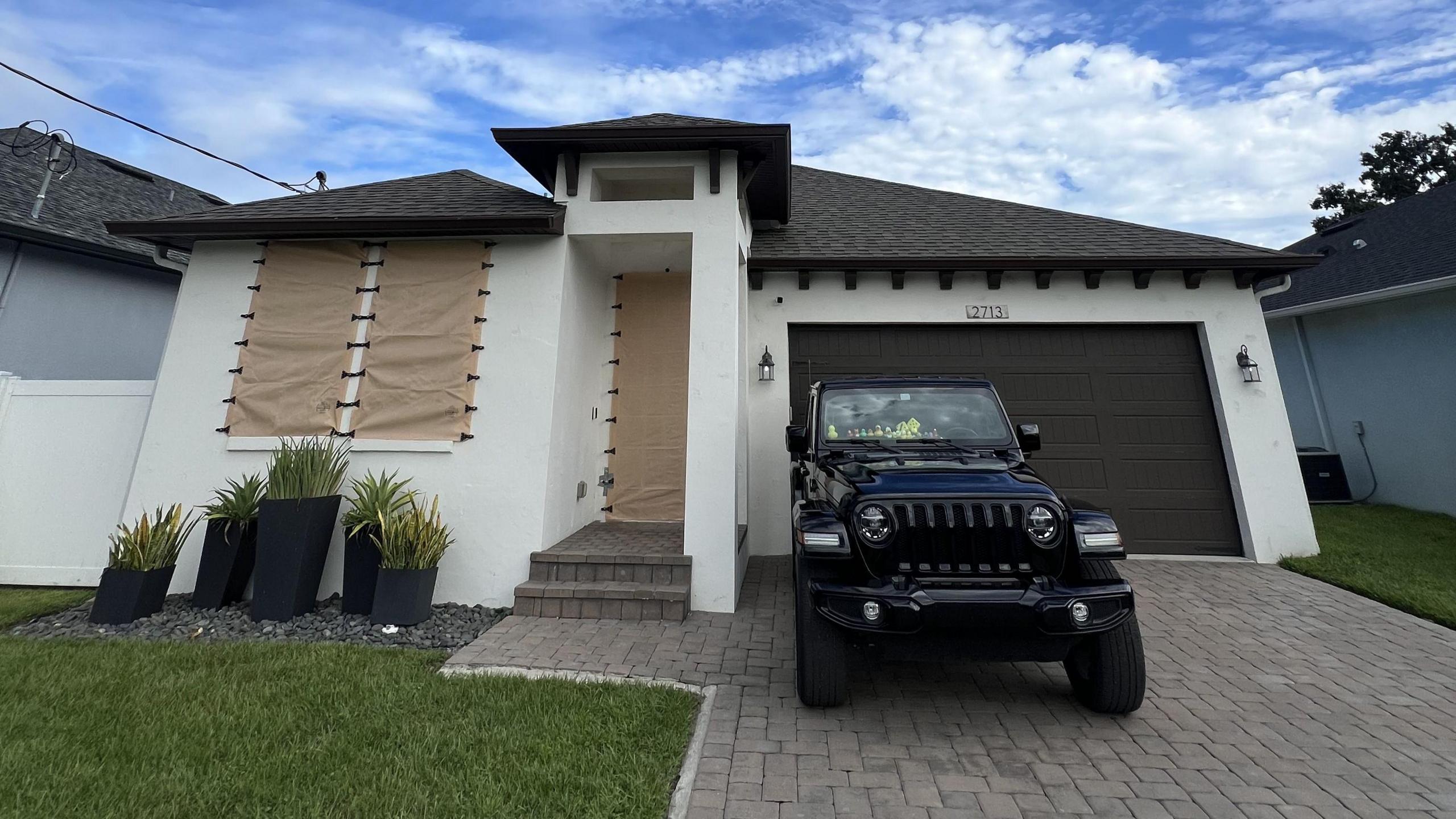 A house with windows temporarily hidden by Kevlar coverings, and with a vehicle parked outside 