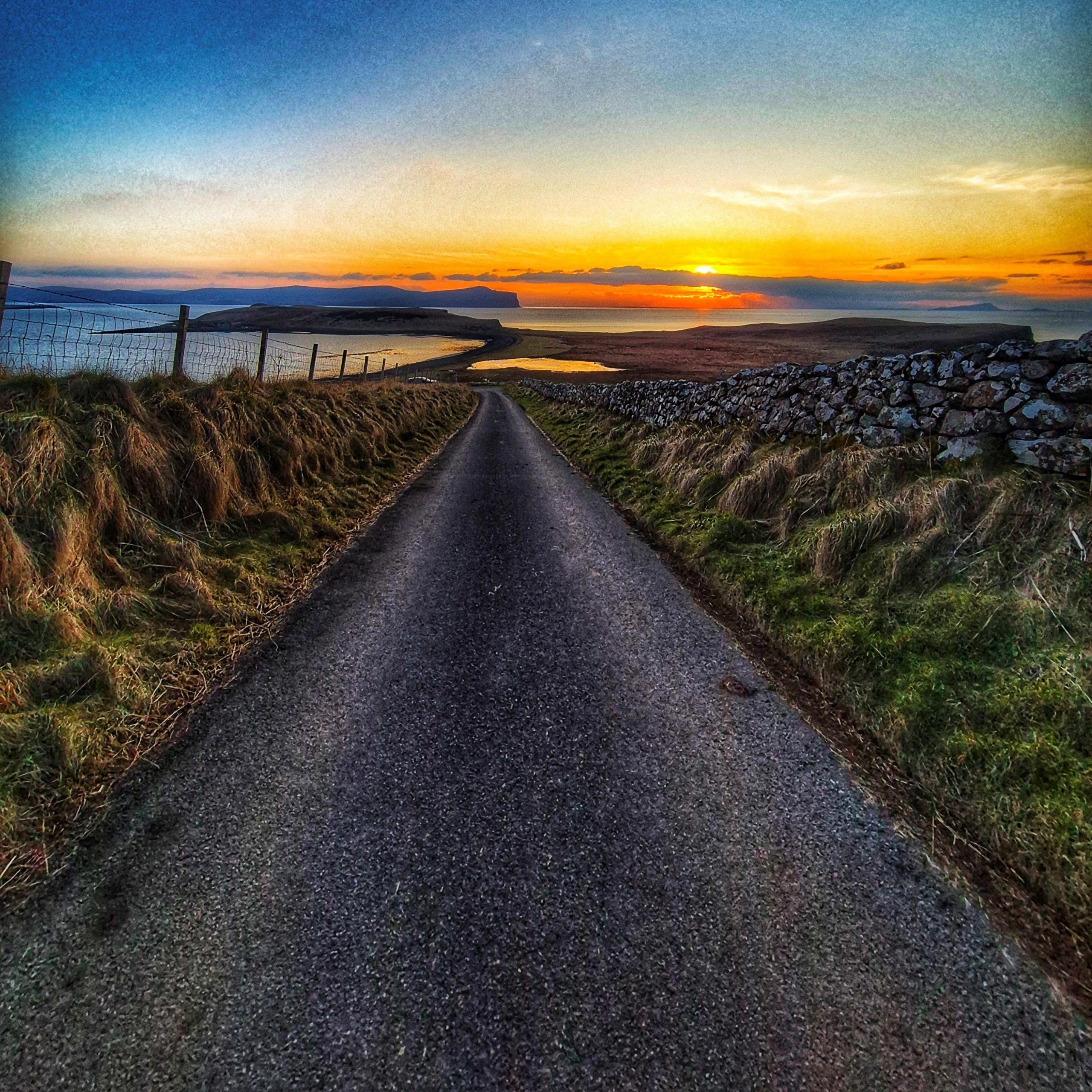 A long straight road with a sunset in the distance.