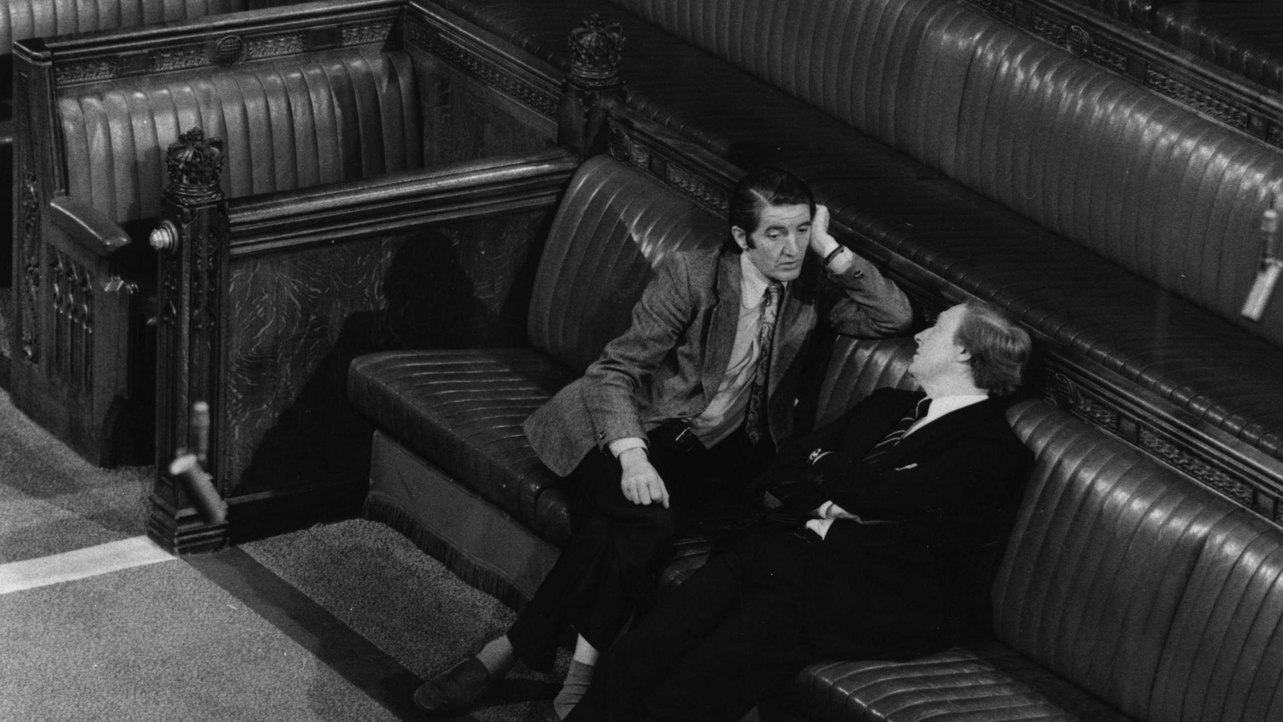 Dennis Skinner sitting on the House of Commons benches in conversation with fellow Labour MP Neil Kinnock in 1977