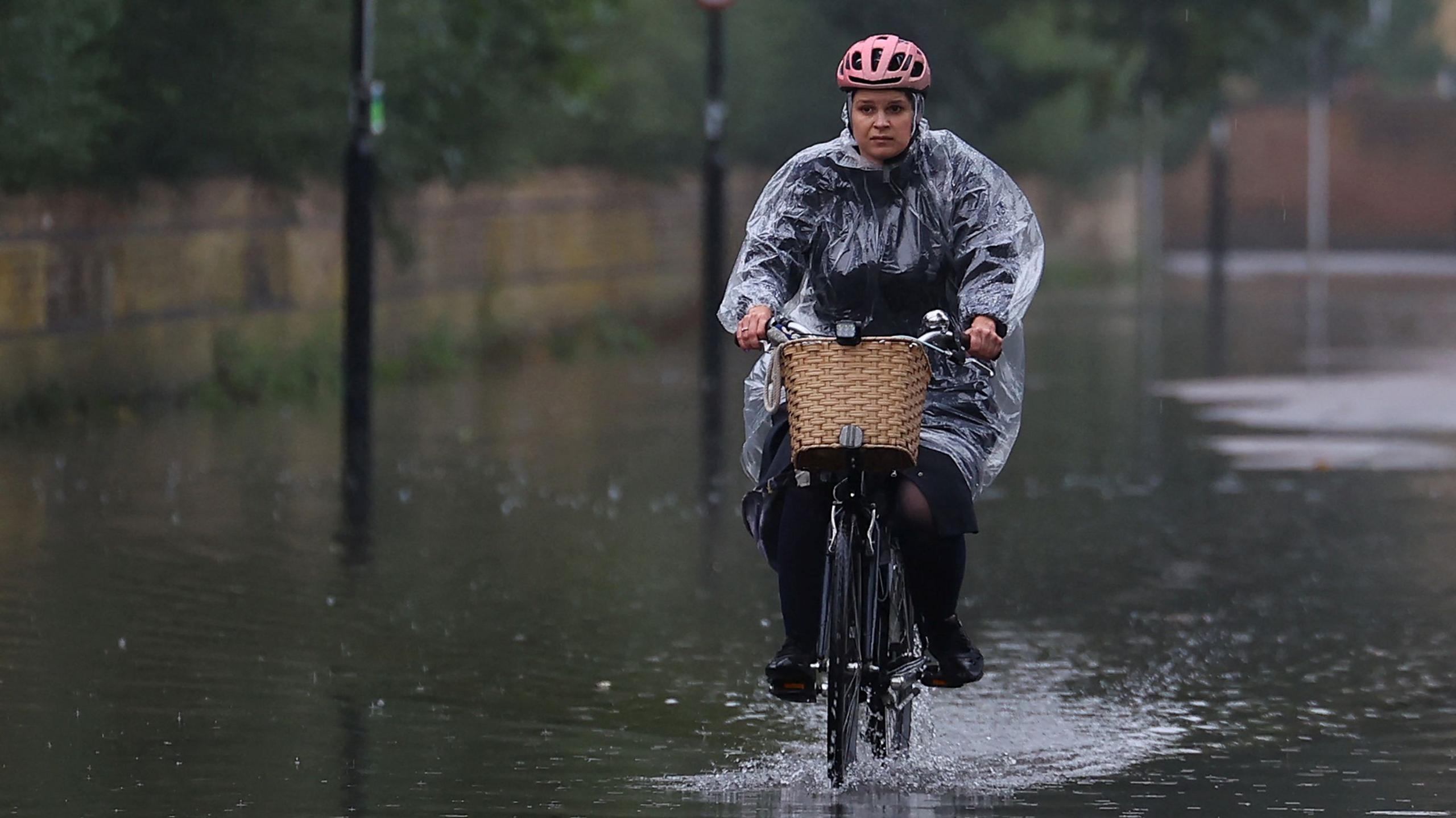 A woman wearing a plastic ran poncho cycles through floodwater after the River Thames overtopped its banks in London