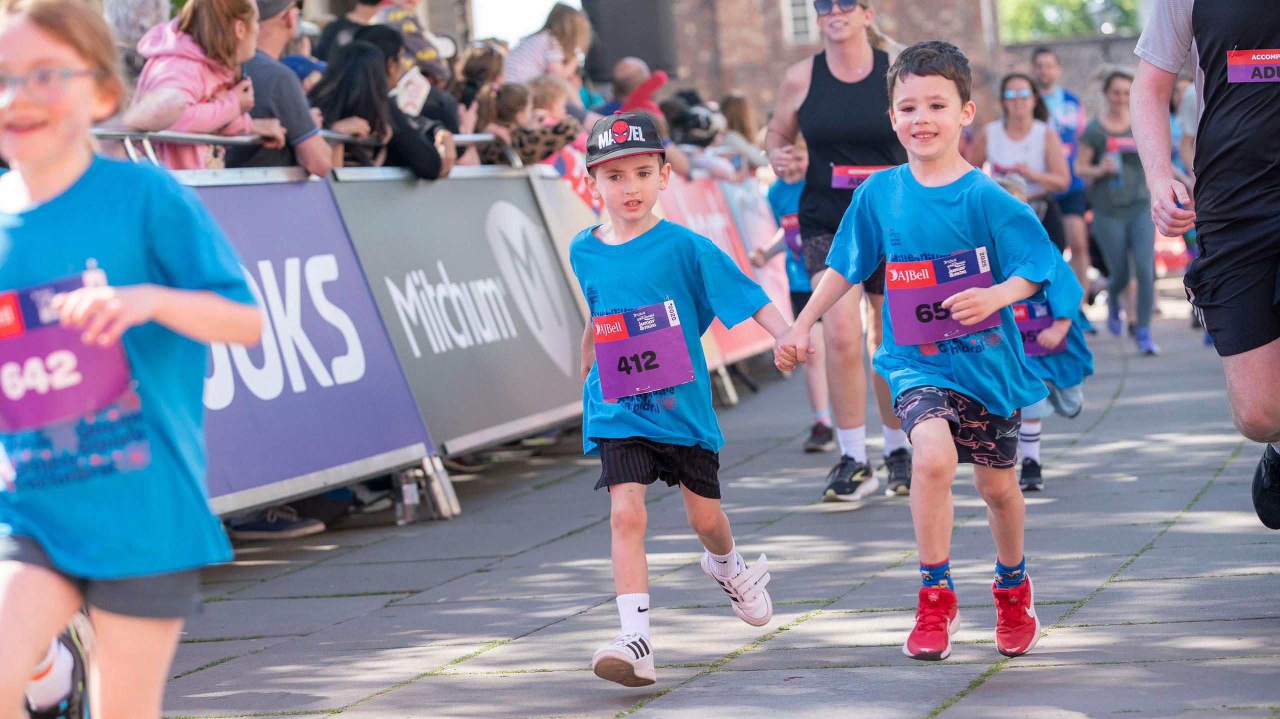 Two young boys both in blue tops run holding hands in the AJ Bell Great Bristol Run juniors event