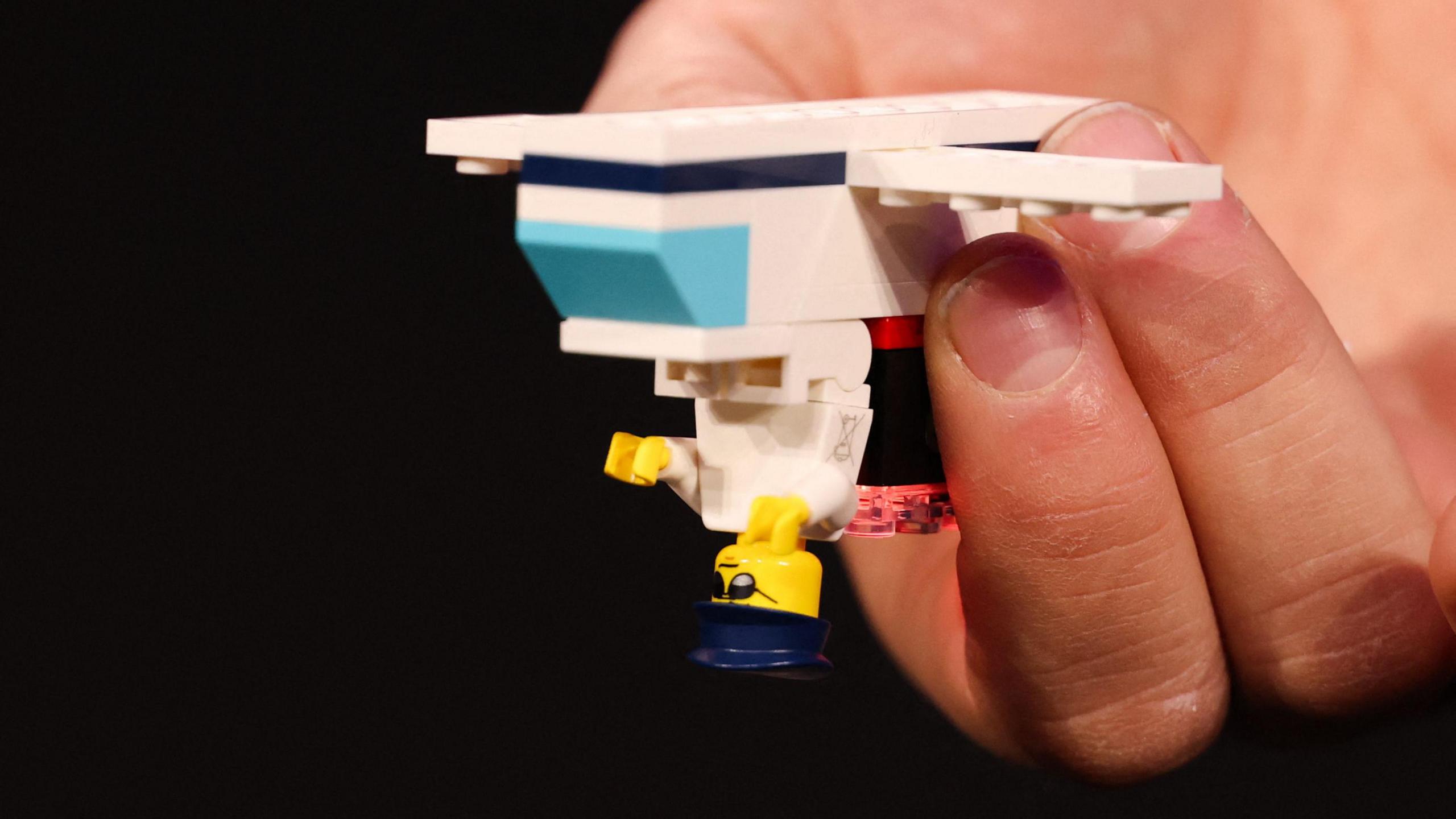 A person holding a simple Lego build of a plane with a pilot upside down