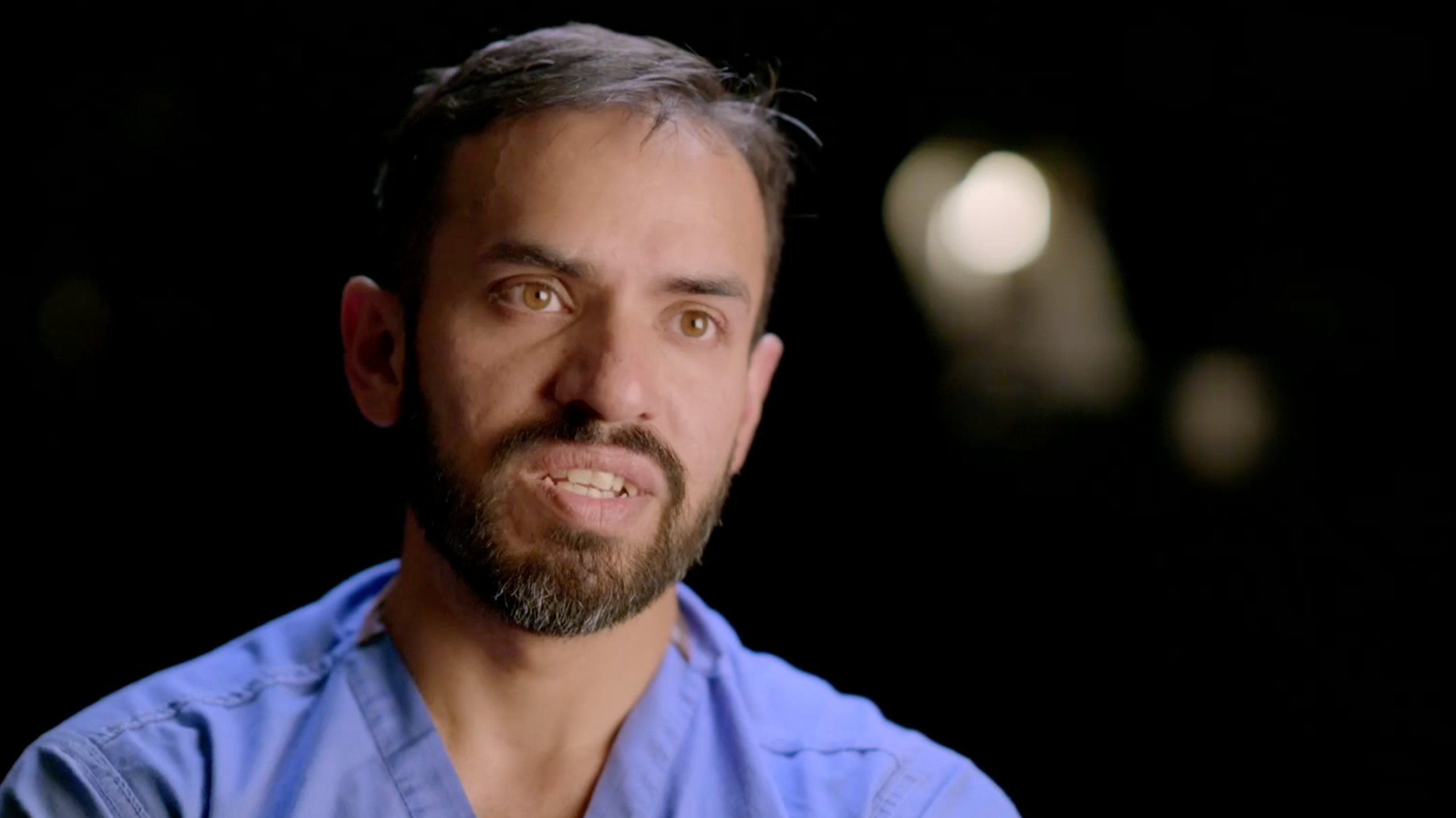 A mid-shot of Mr Akbar Hussain, a neurosurgeon at Newcastle Hospitals. He is pictured wearing his blue surgical scrubs.
    