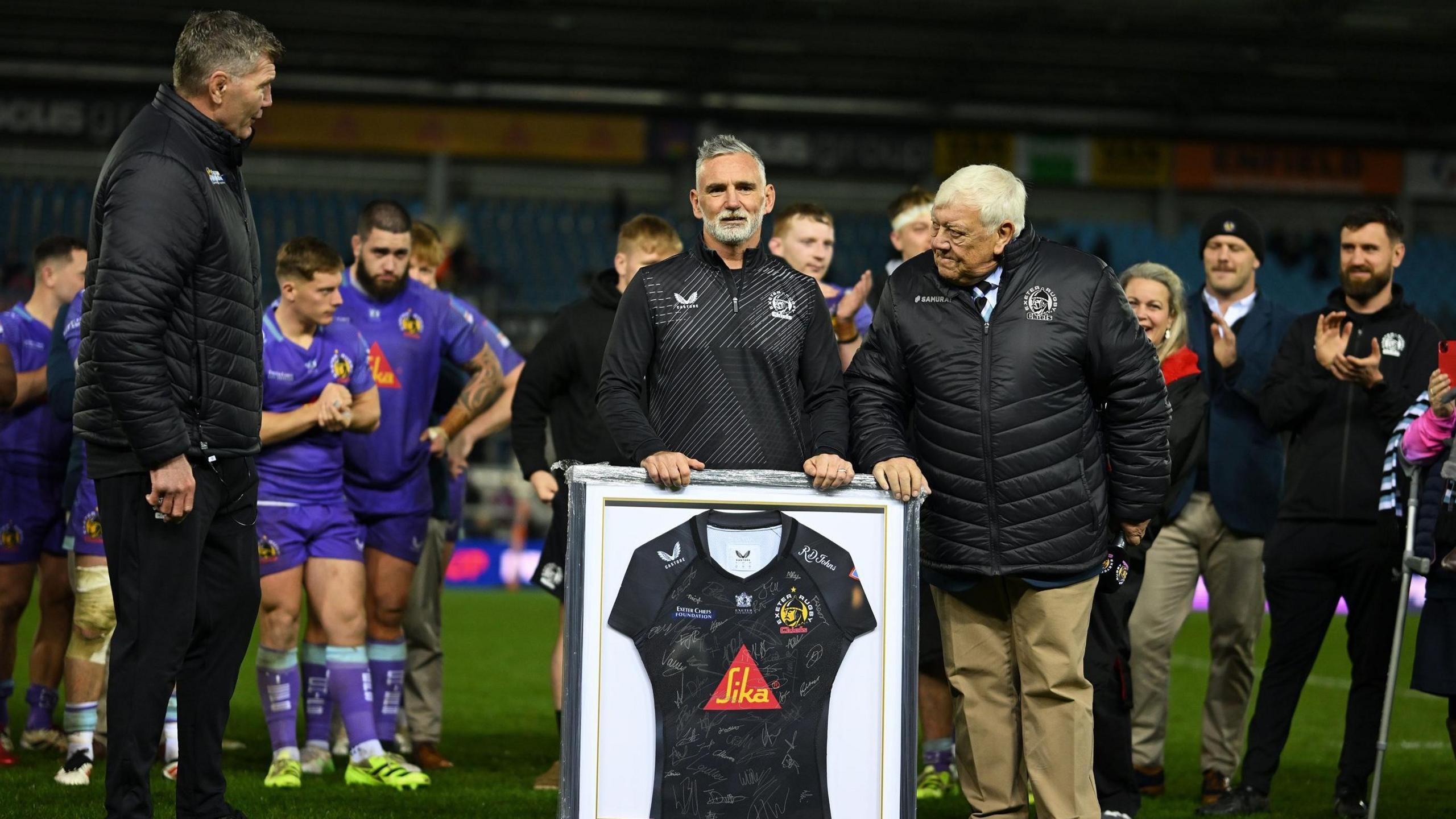 Exeter's director of rugby Rob Baxter (left) and chief executive Tony Rowe (right) present Pellow with a framed shirt on the field after the game