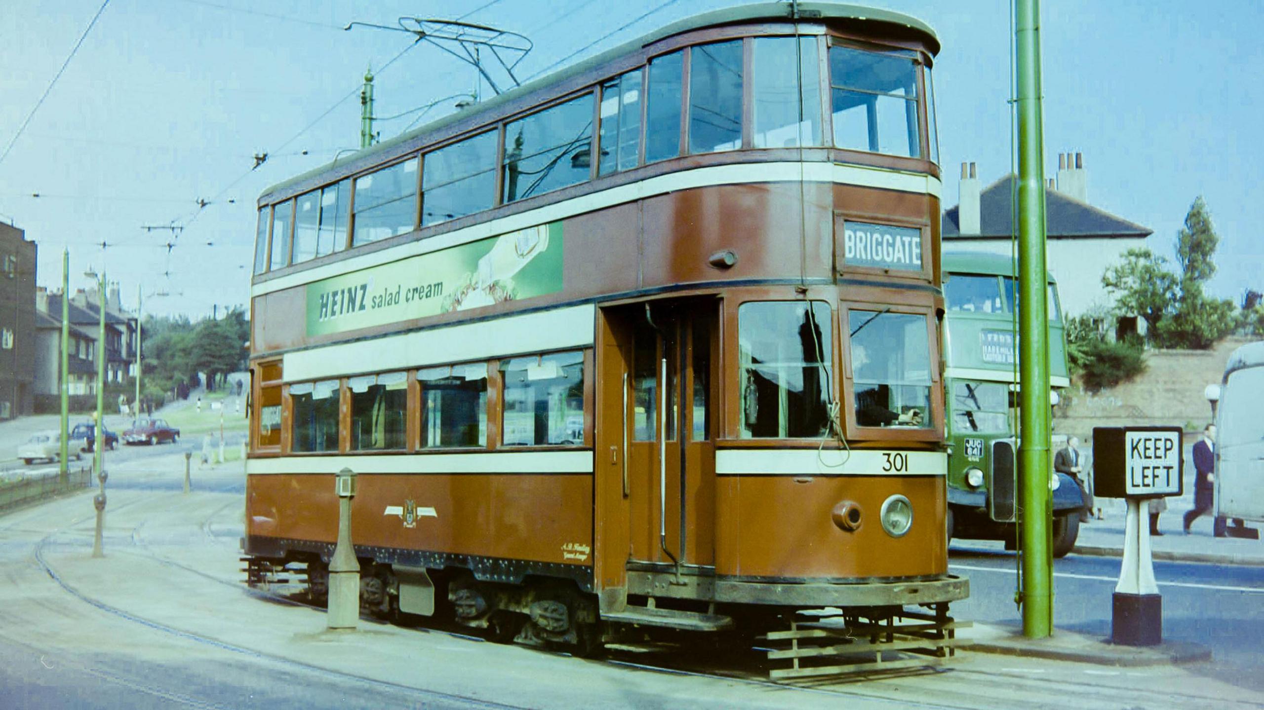 A red-coloured tram in motion on a city street in the 1950s. The tram's destination, signposted on the front of the vehicle is Briggate. An advert for Heinz salad cream runs along the side of the tram car. 