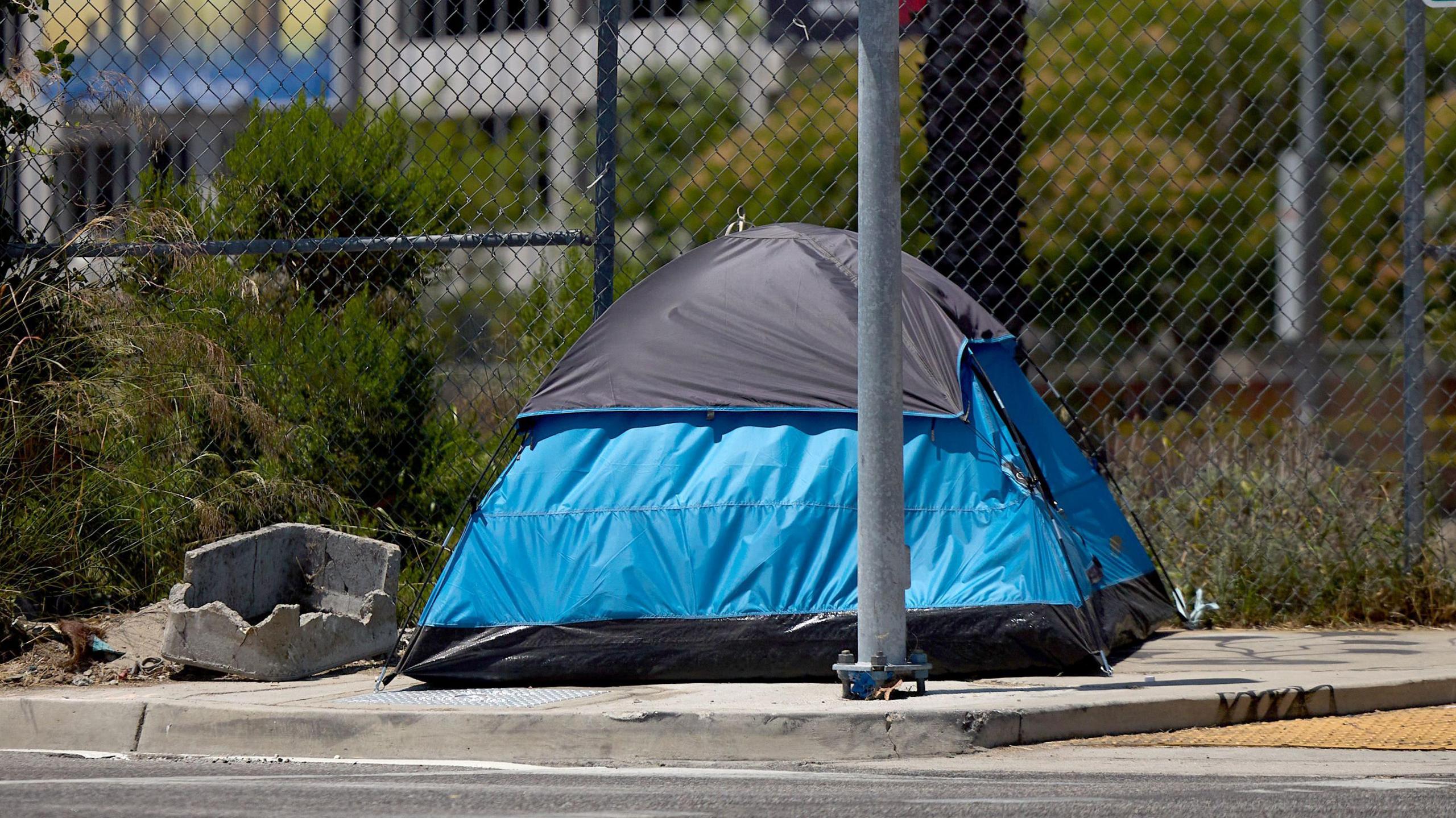 A blue tent housing a homeless person is set up on the sidewalk in Los Angeles, California 