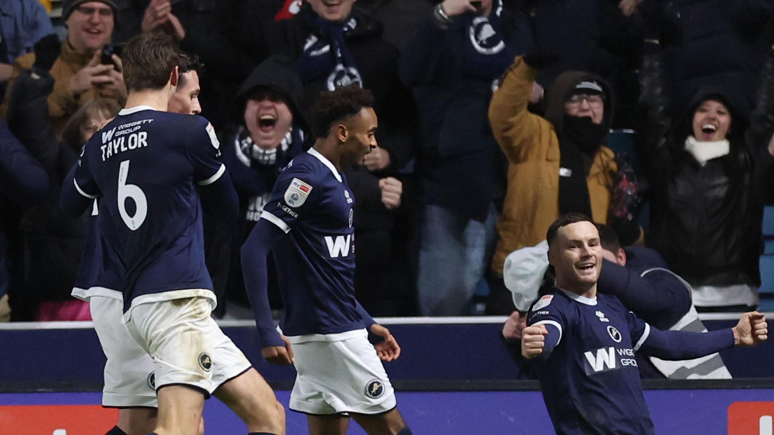 Macaulay Langstaff celebrates with a knee slide and arms outstretched as Millwall team-mates run behind him to congratulate him