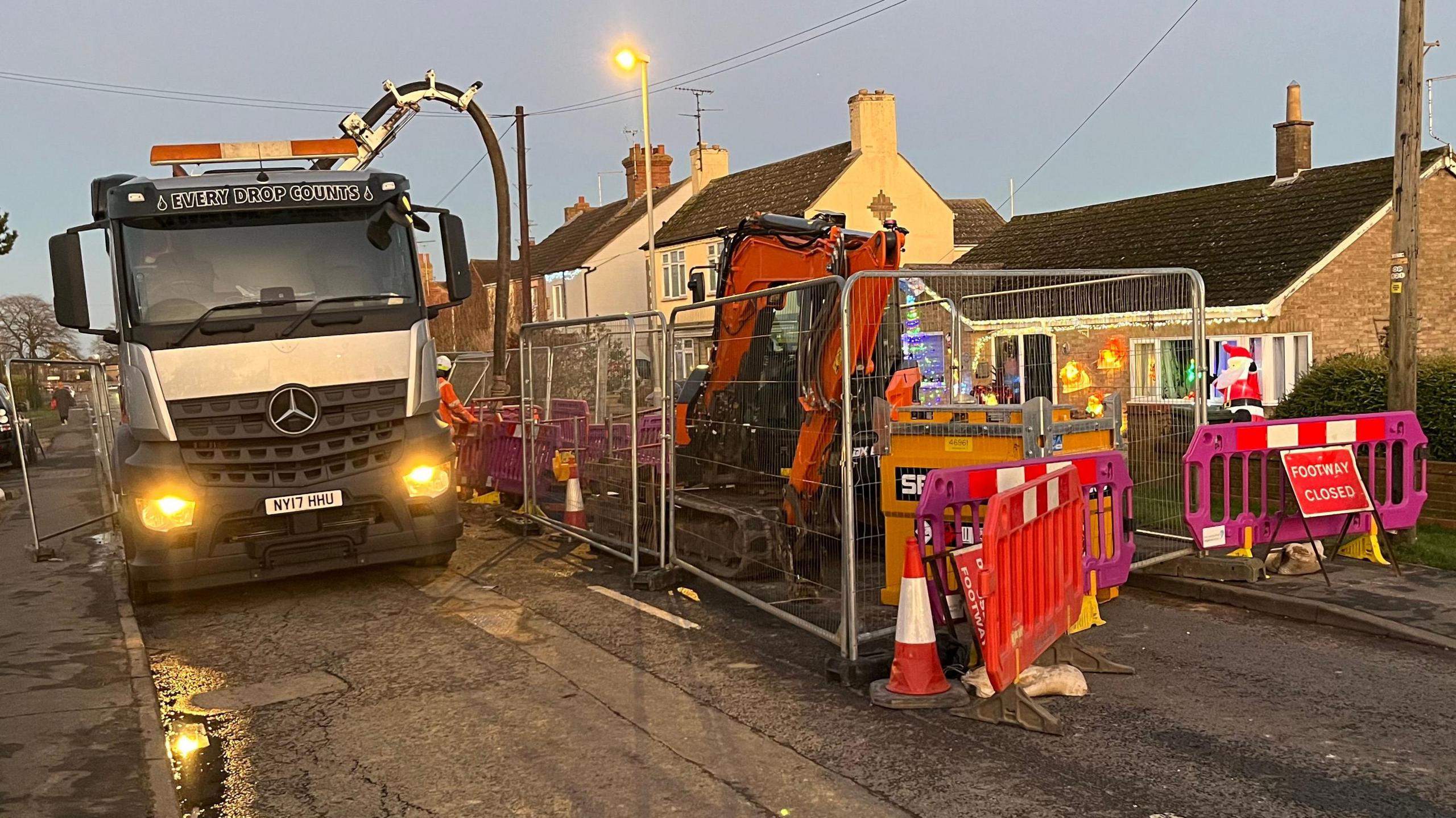 A white lorry on the road next to work equipment, including an orange digger and road diversion signs