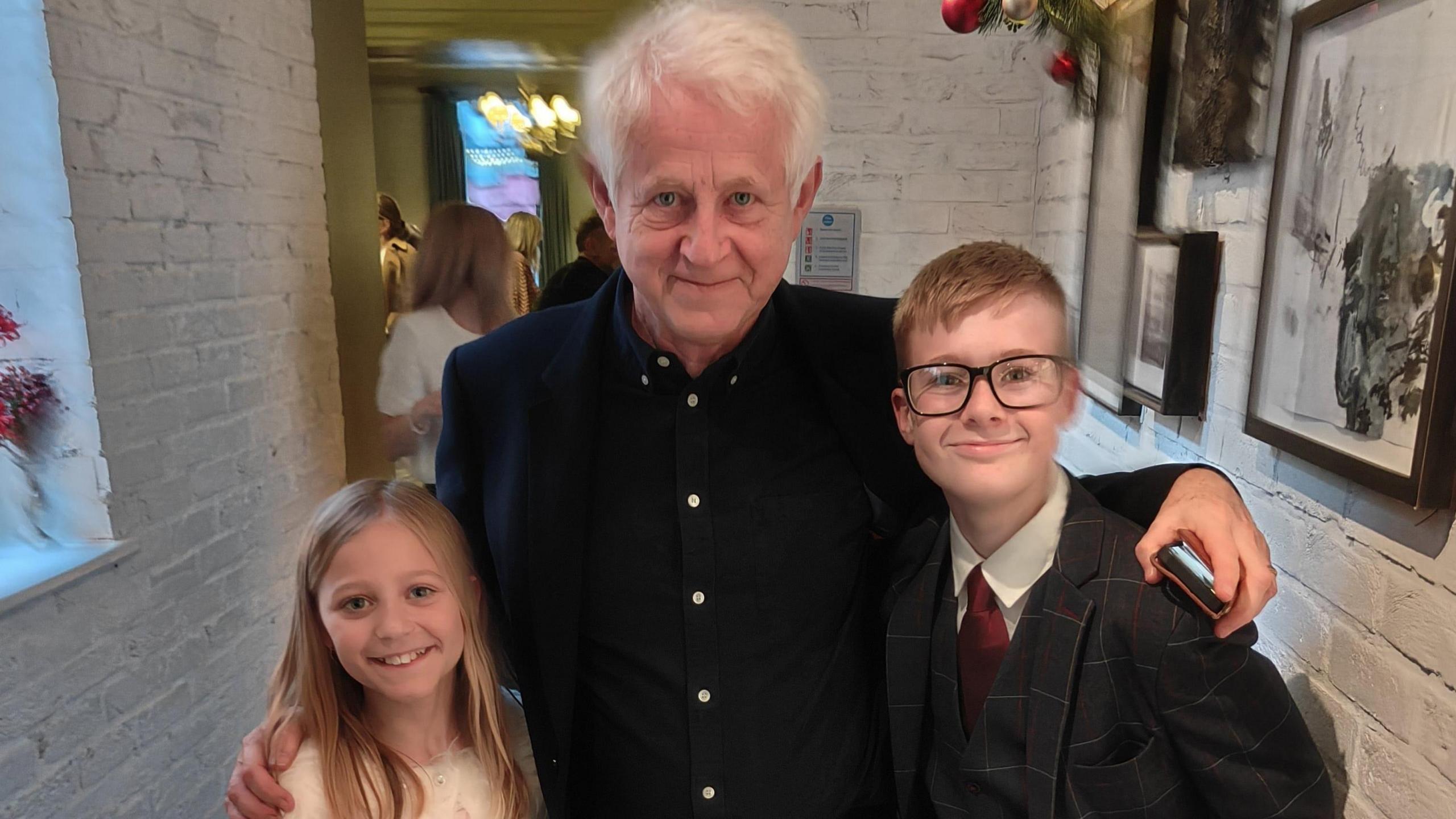 Director Richard Curtis (centre) wearing a black shirt, with Jack on his right hand side in a suit and black glasses, and Jack's younger sister on the left. 