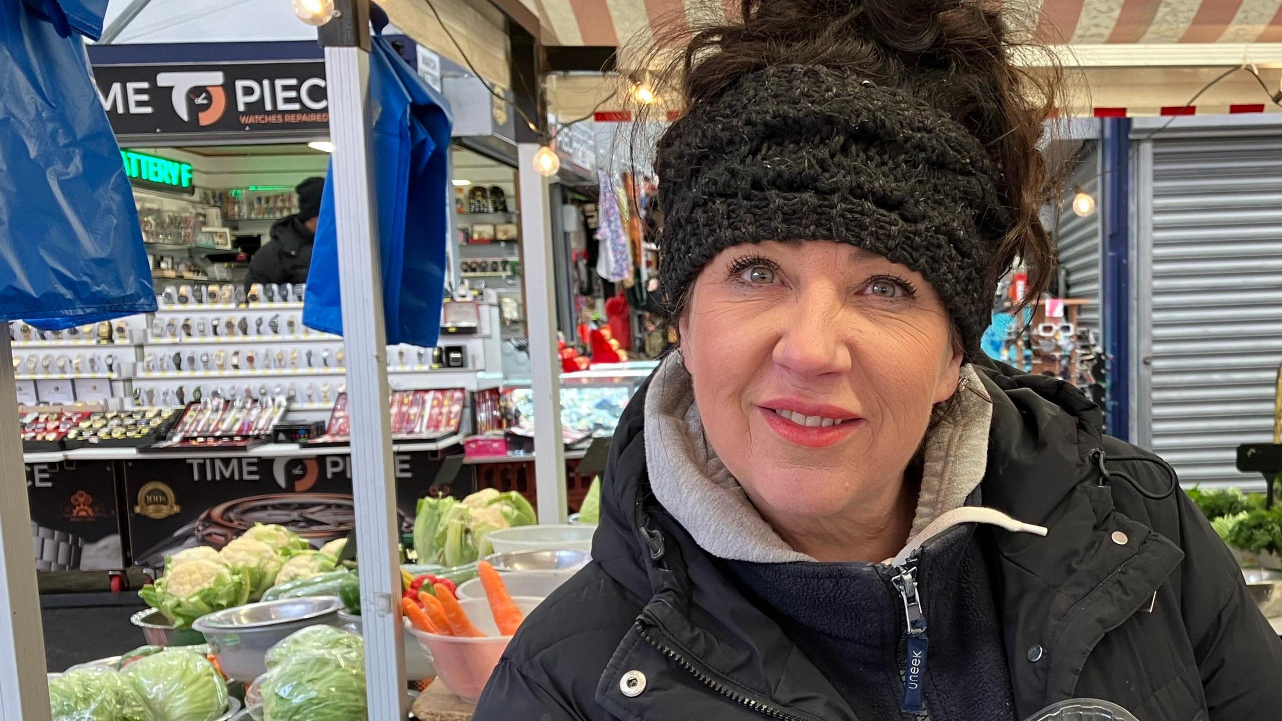 A woman in front of lettuces, cauliflowers and carrots