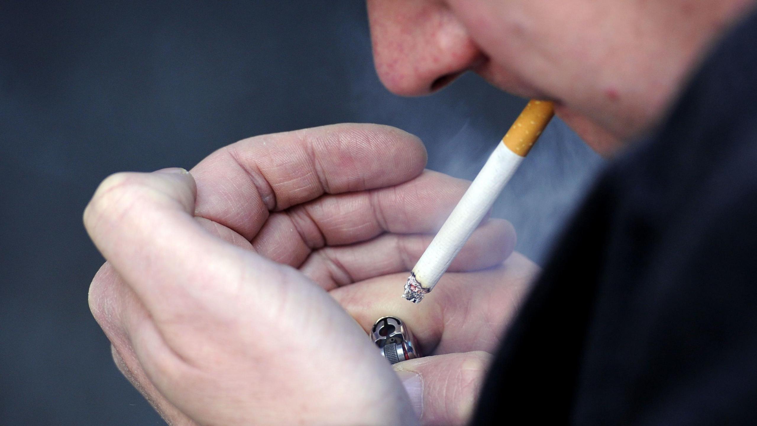 Close up of a man lighting a cigarette using a lighter. 