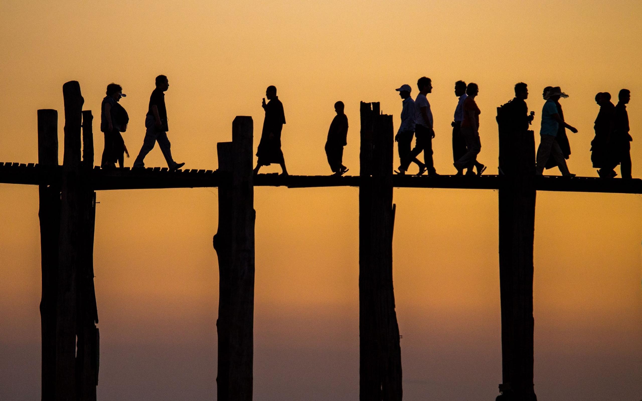 People walk across a bridge against a sunset