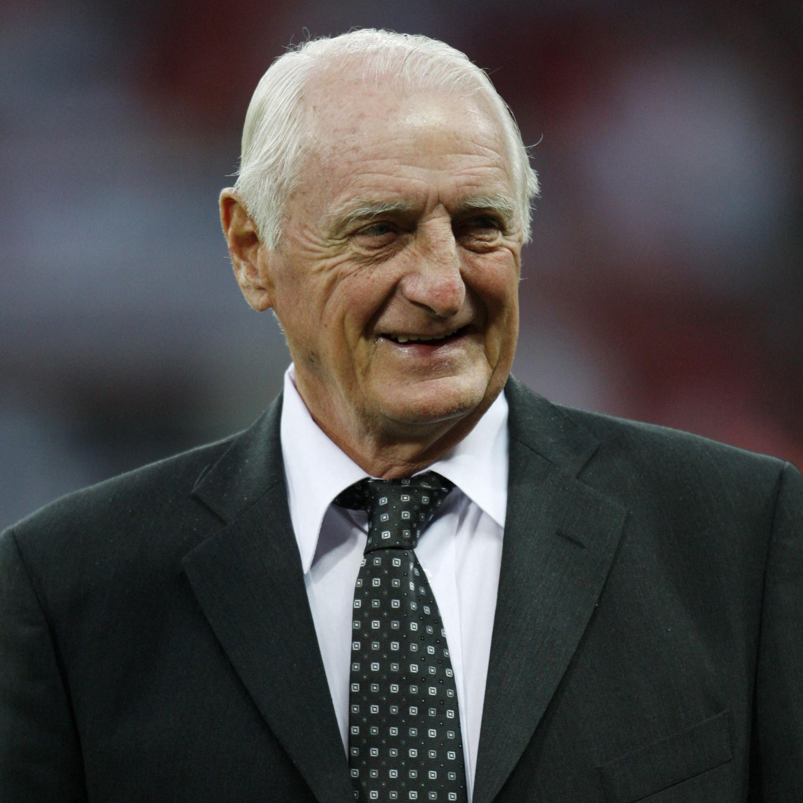 George Eastham smiling while wearing a black suit jacket, black tie with small white shapes, and a white shirt.