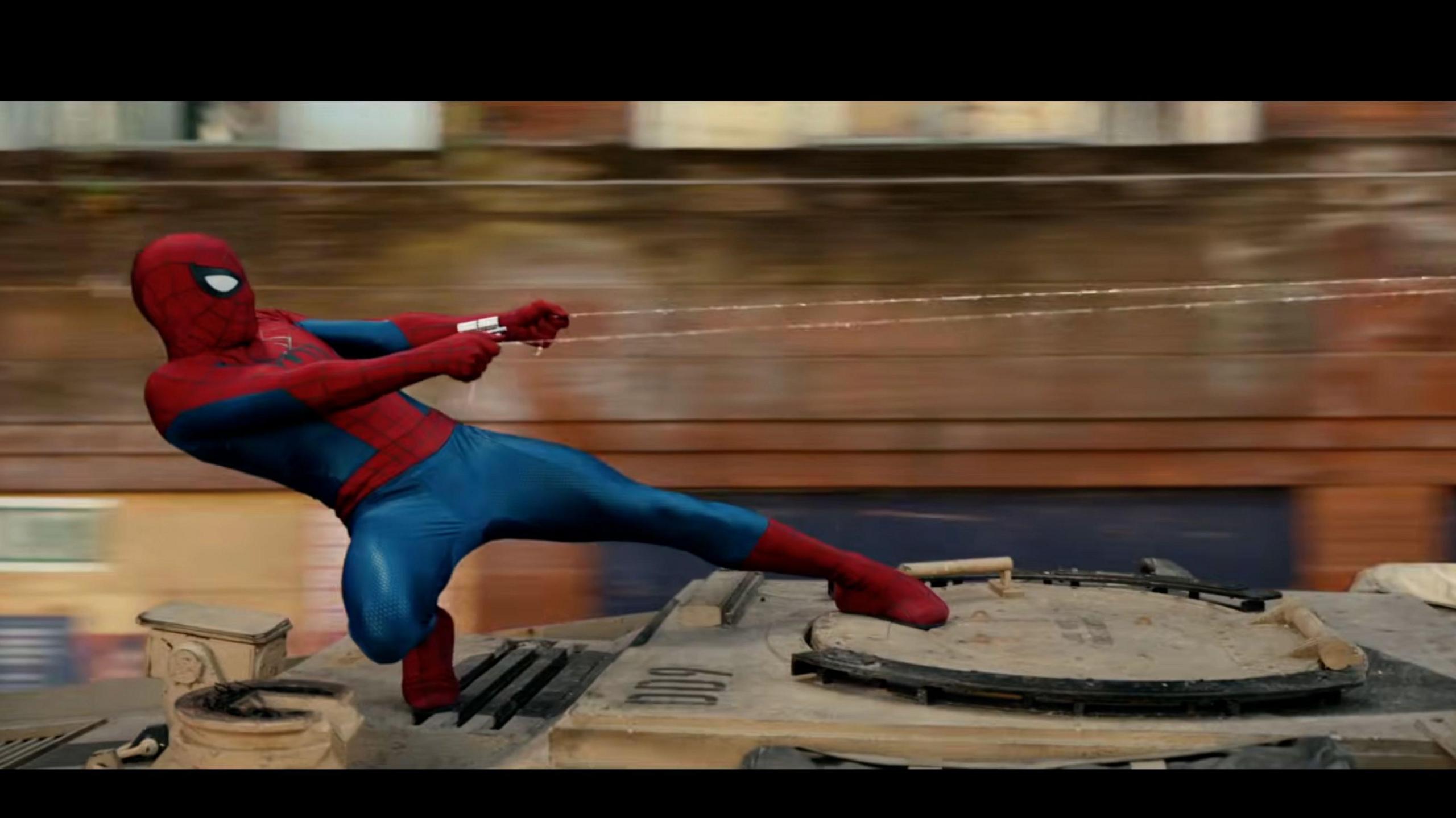 Spider-Man using his webs while stood on a moving tank.
