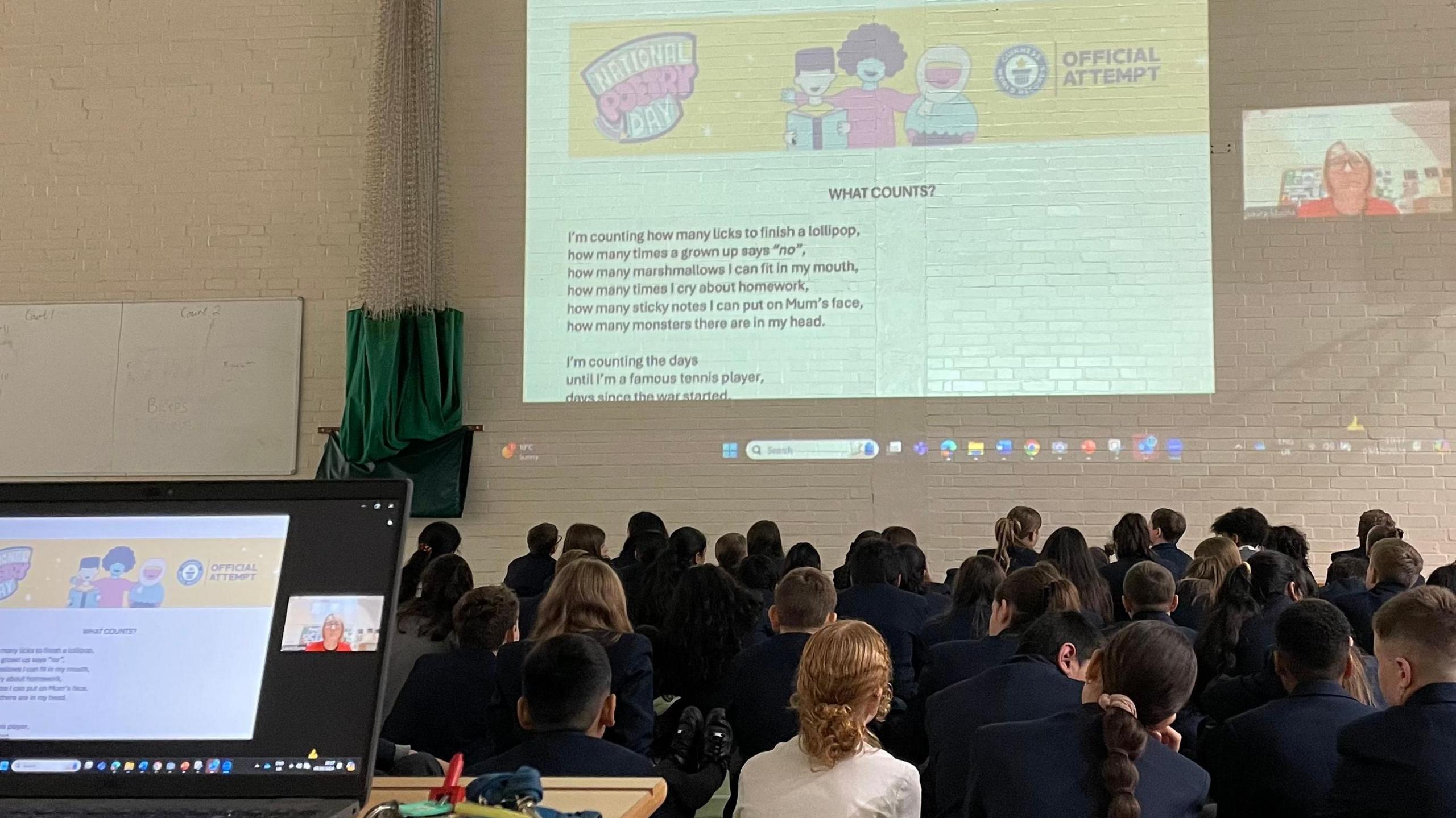 Children from Roundhill Academy sit in their school hall looking up at a projection of the words in the poem they are creating.
