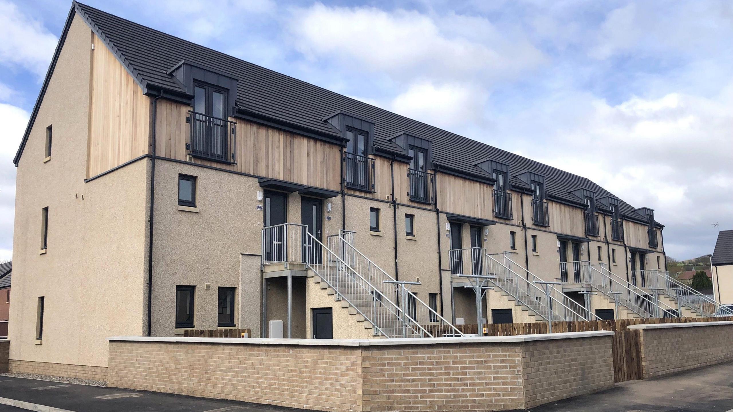 A row of houses in brick and wood with staircases and metal railings leading up to their front doors