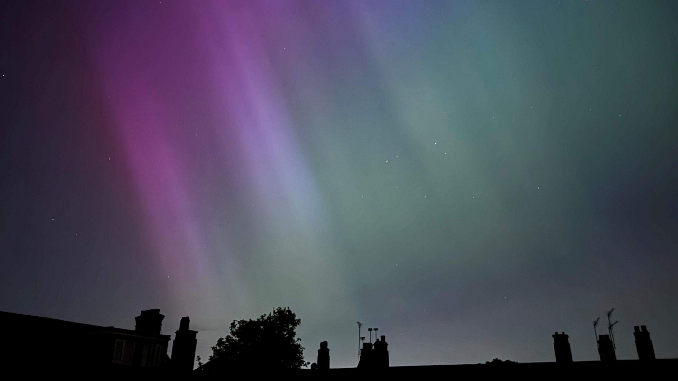 Purple and green Northern Lights over rooftops