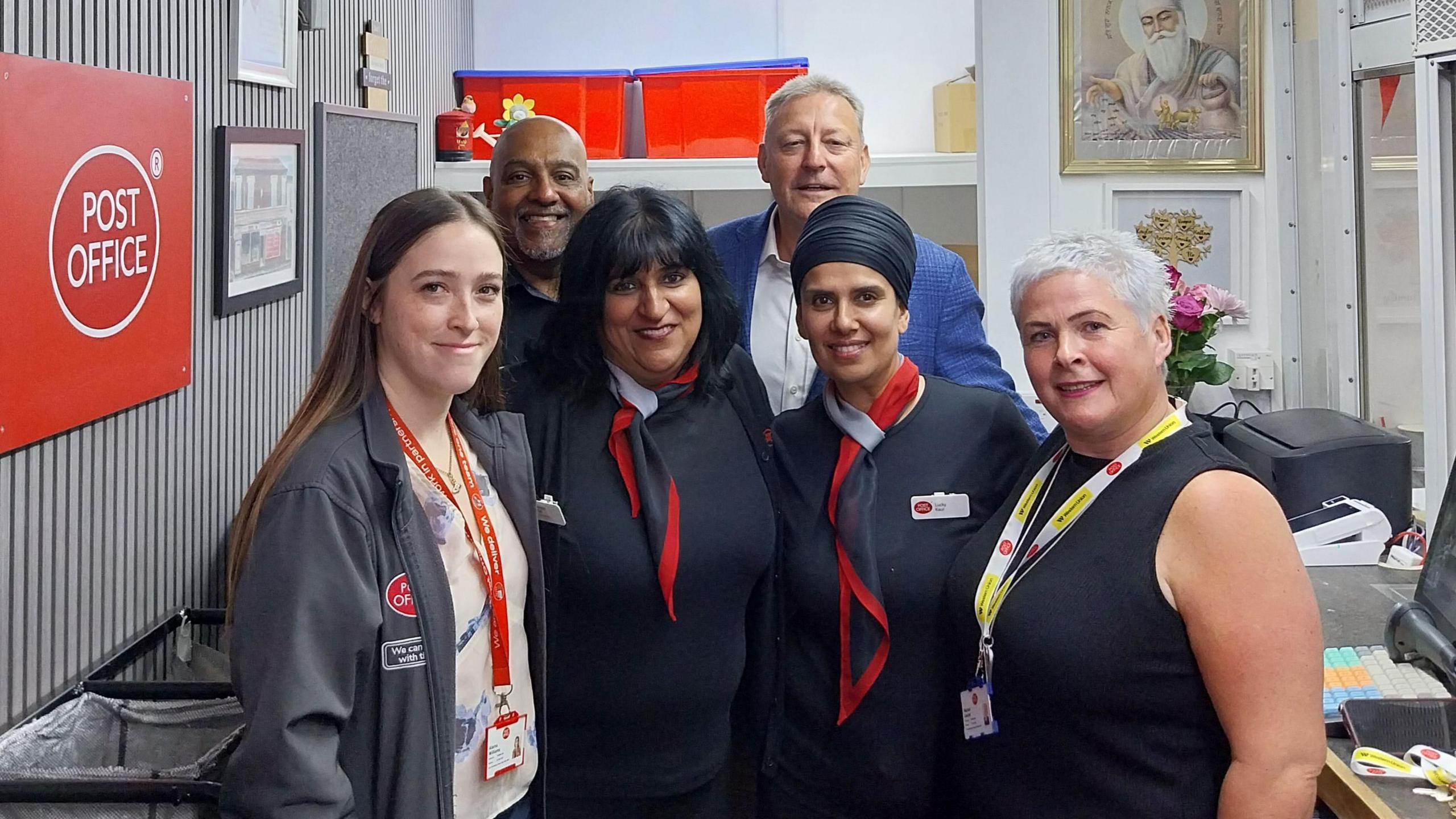 Ms Gill with staff inside the Post Office. Post Office chairman Nigel Railton is stood behind the staff members wearing a bright blue suit. 