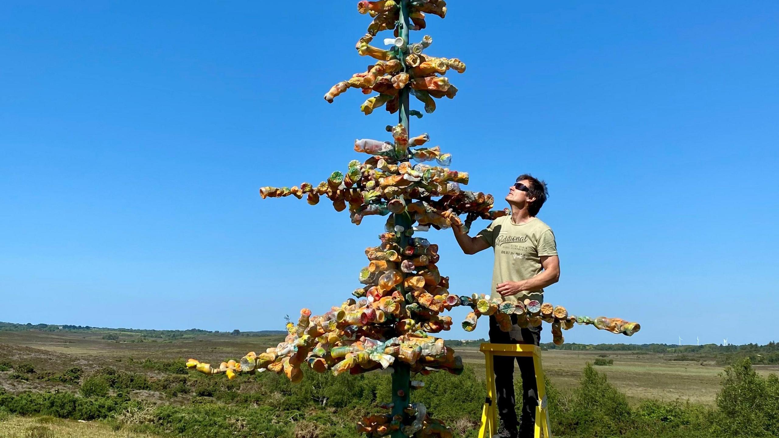 Plastic bottle sculpture and Robert Marshall next to it on a ladder adding bottles