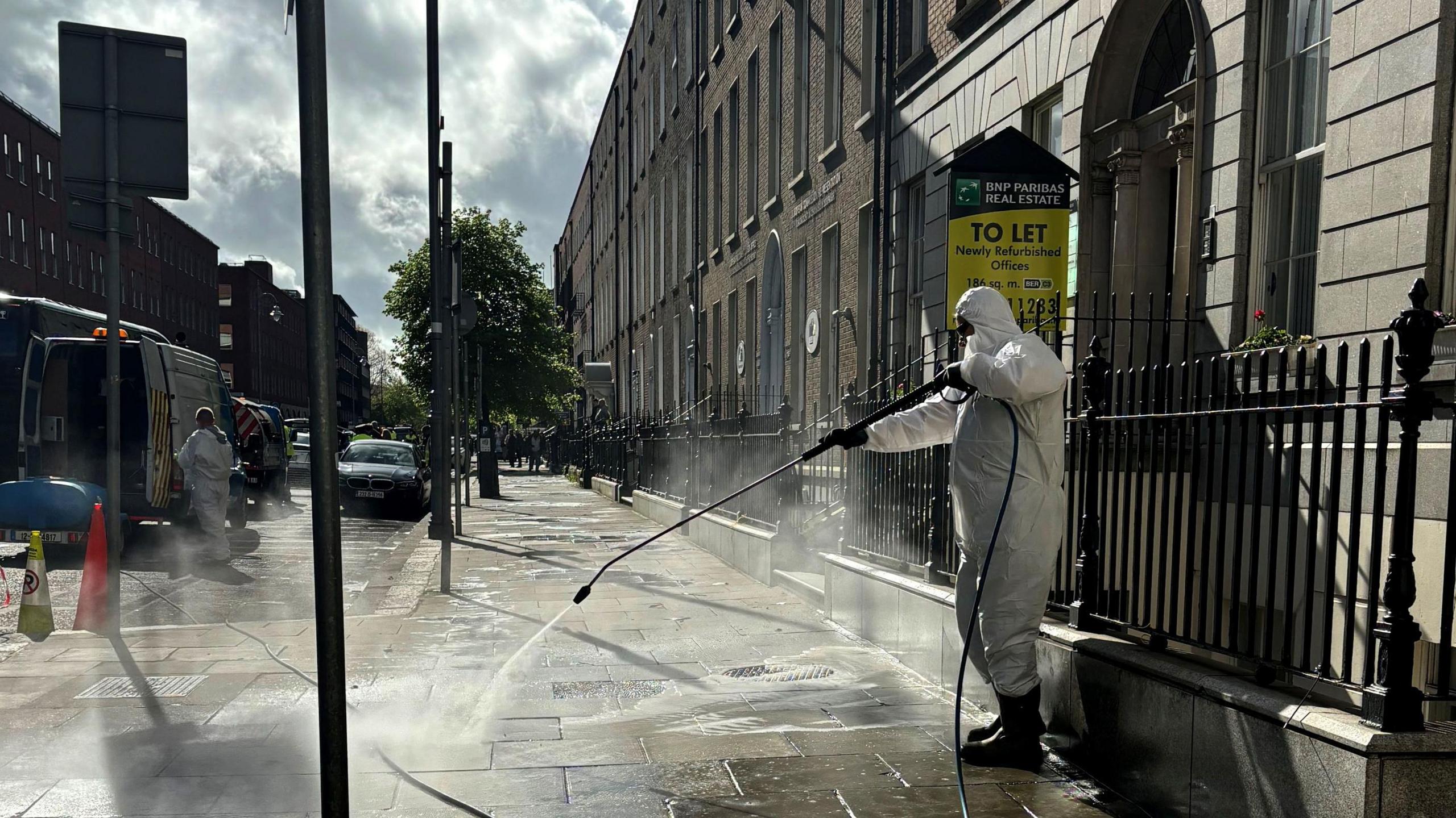 A cleaner in a white protective suit power washing Mount Street after the encampment was cleared.