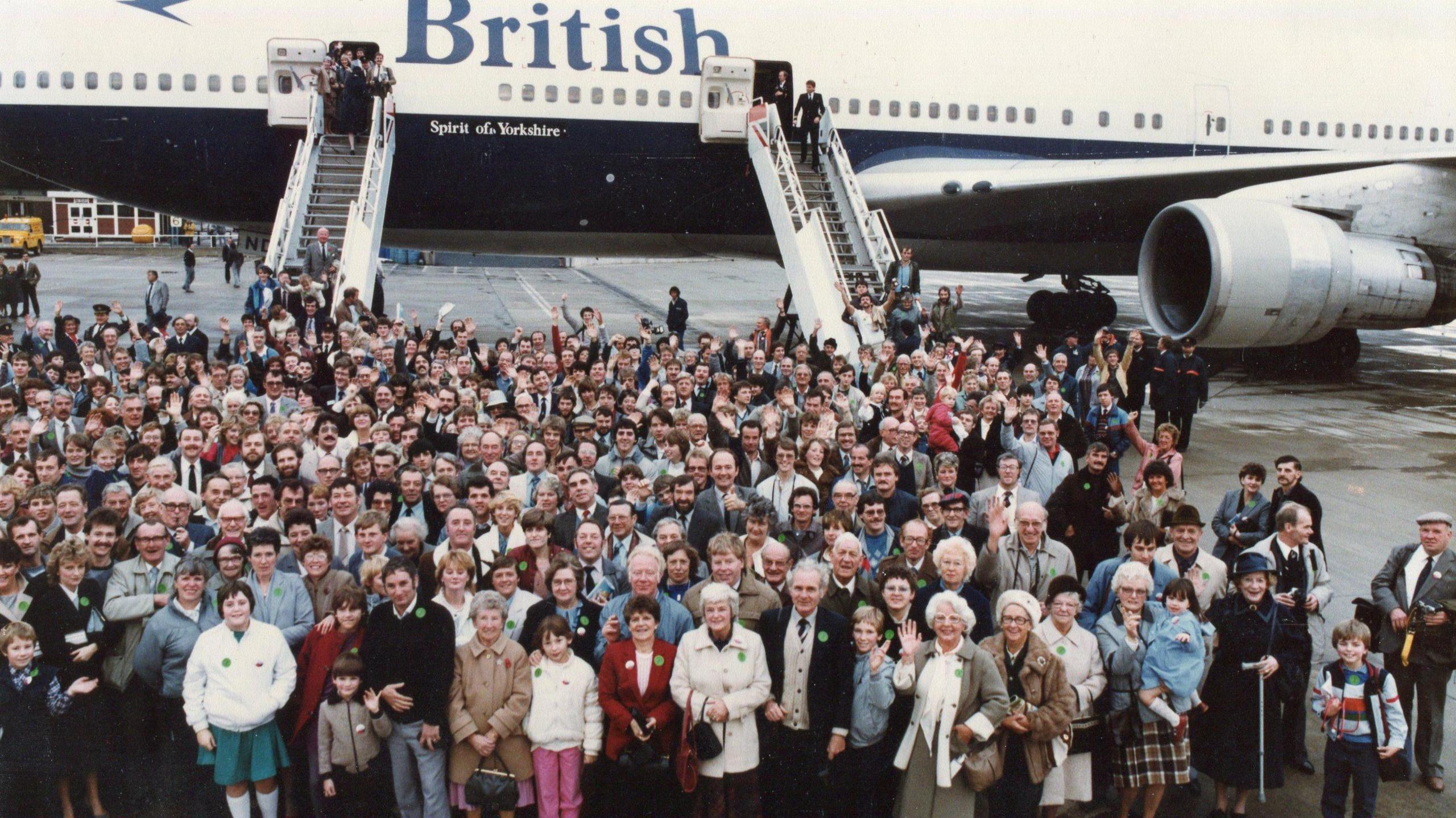 Hundreds of people lined up on the tarmac in front of a blue and British Airways Boeing 747 jumbo jet.   