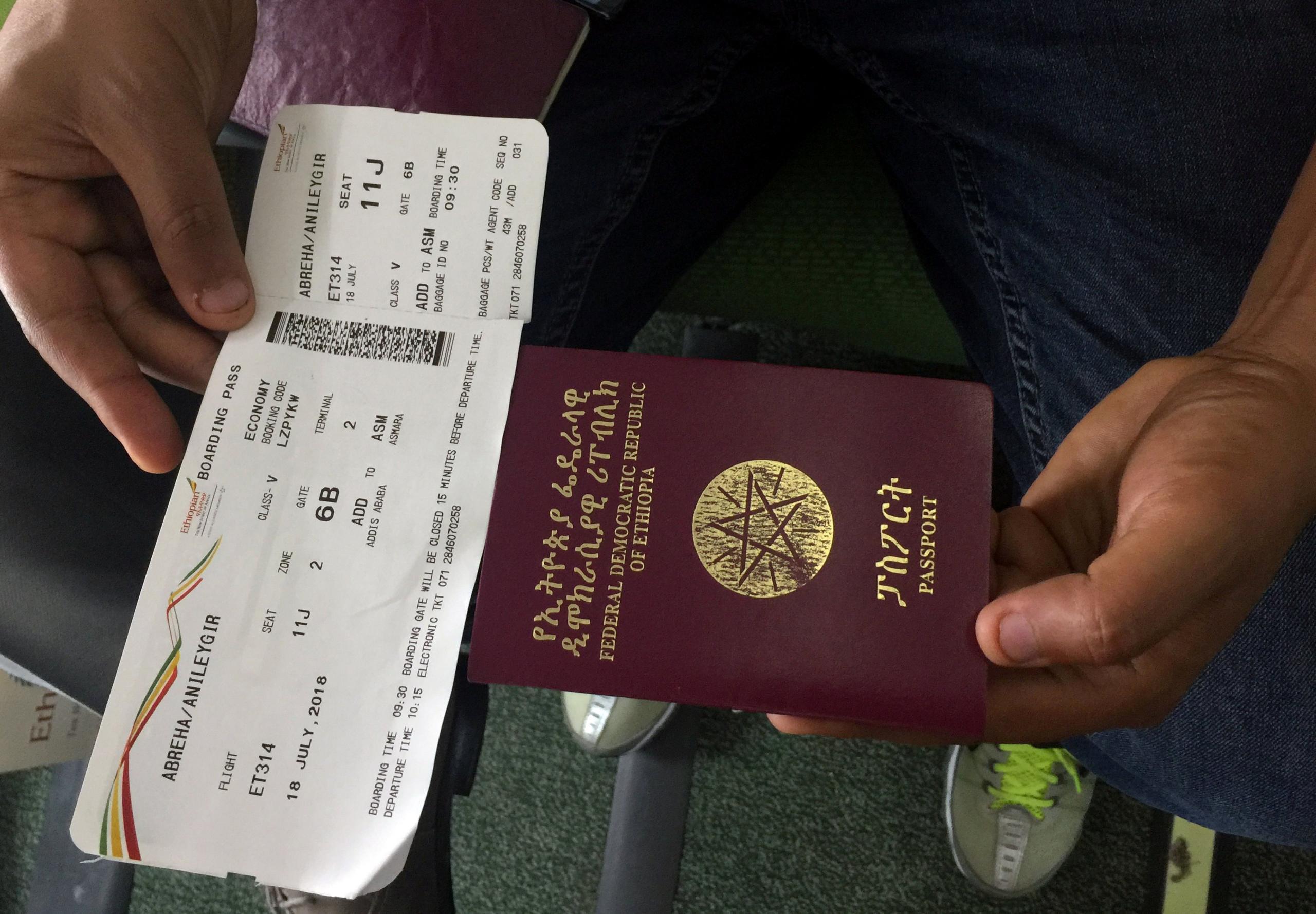 A passenger displays an Ethiopian passport and an Ethiopian Airlines boarding pass as he sits inside ET314 flight to Eritrea"s capital Asmara at the Bole International Airport in Addis Ababa, Ethiopia July 18, 2018.