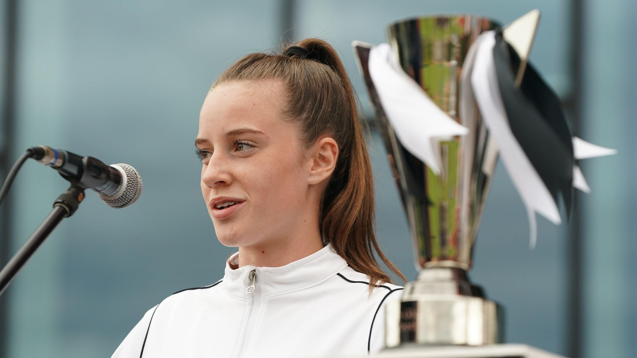 Ella talking into a microphone while standing next to a trophy