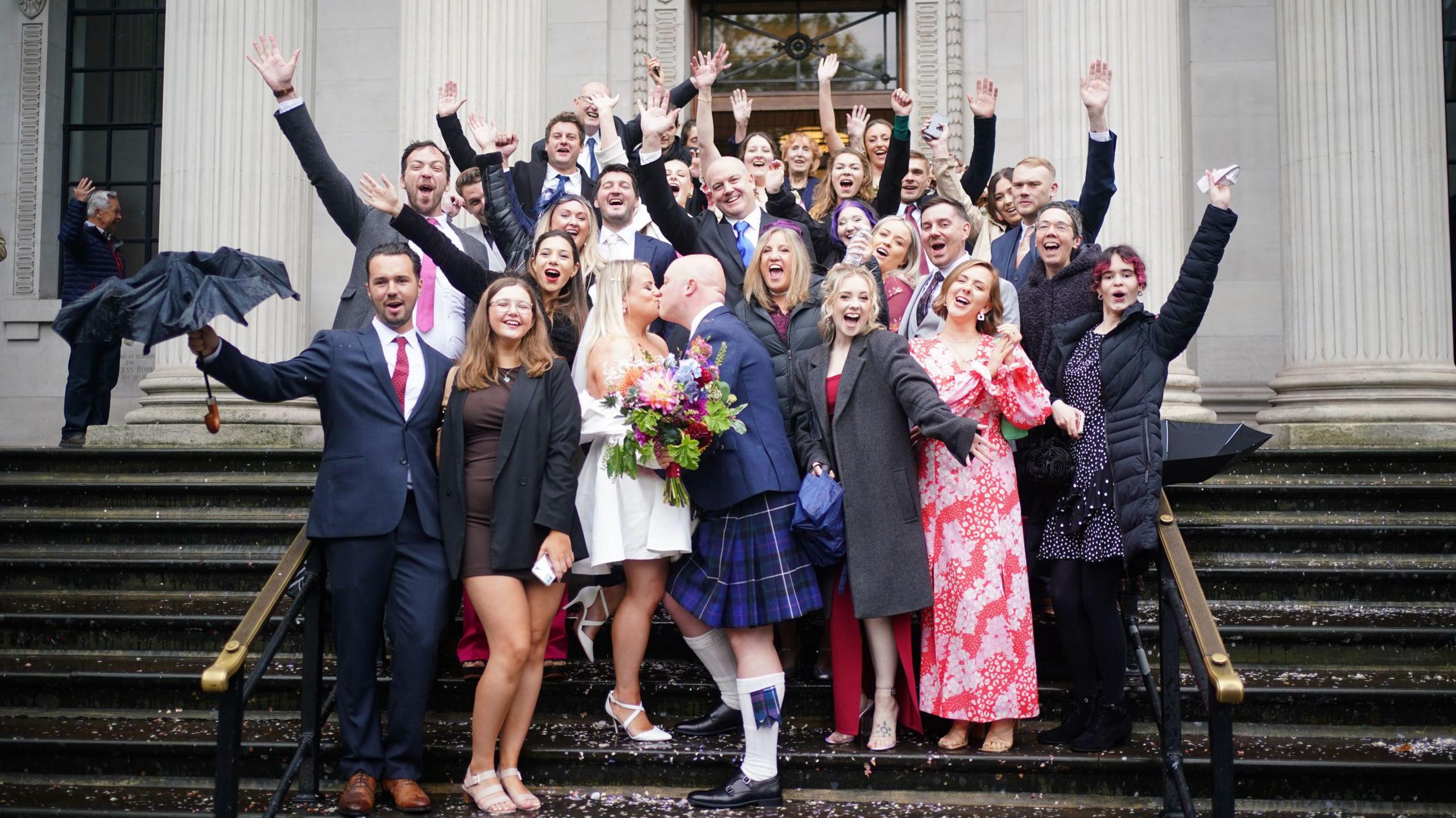 People crowd and cheer on the steps of the old marlyebone town hall as thomas and paige mackintosh celebrate tying the knot on 1 October. Confetti can be seen on the floor while the group have their hands in the air cheering