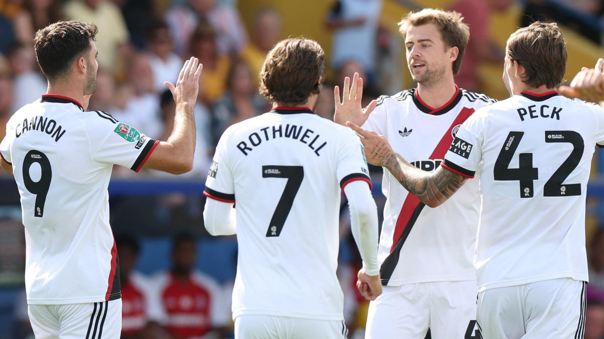 Sheffield United players wearing white kits celebrate Patrick Bamford's goal at Mansfield Town