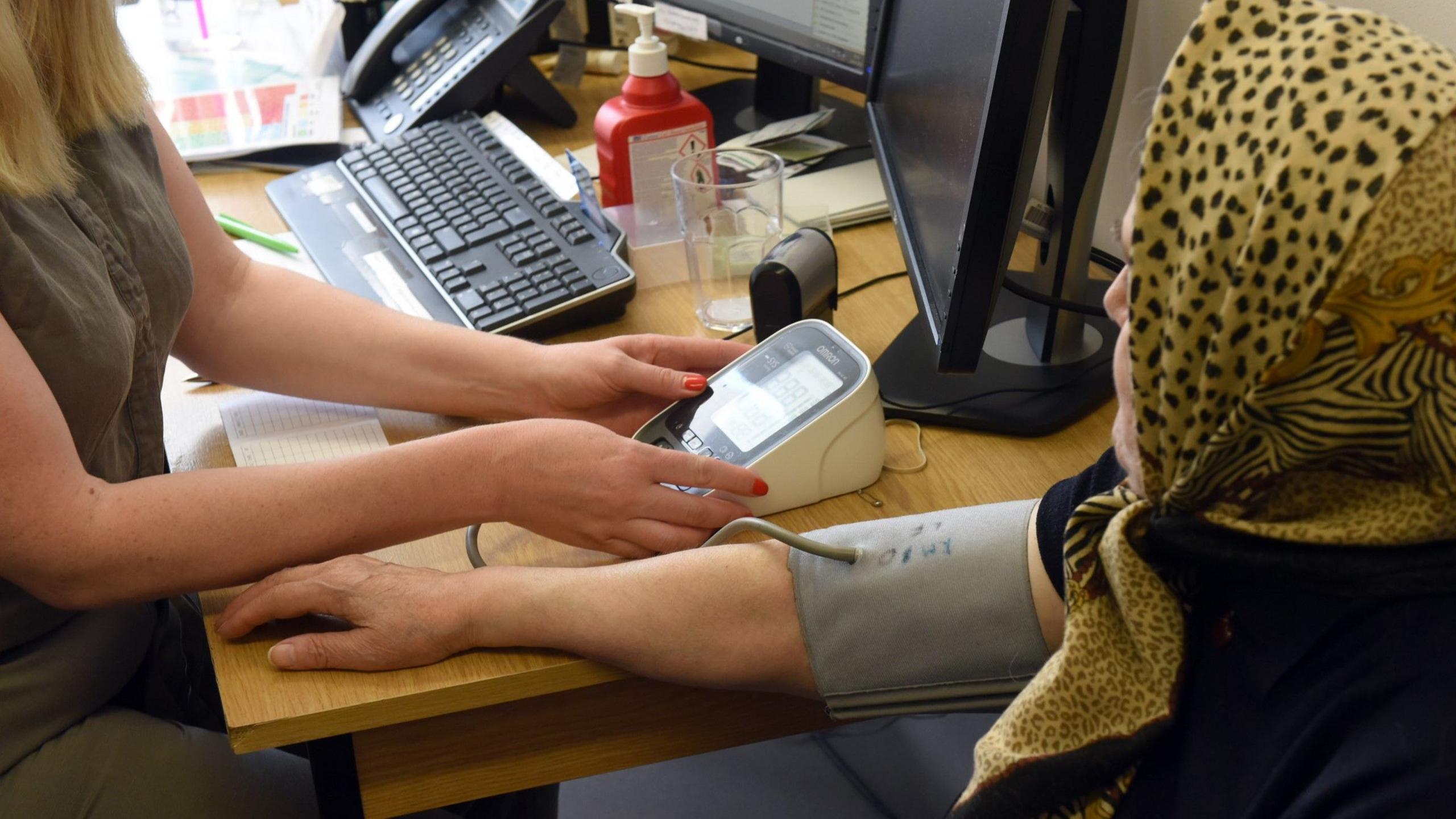 A woman in a patterned headscarf has her blood pressure checked at a GP surgery. 