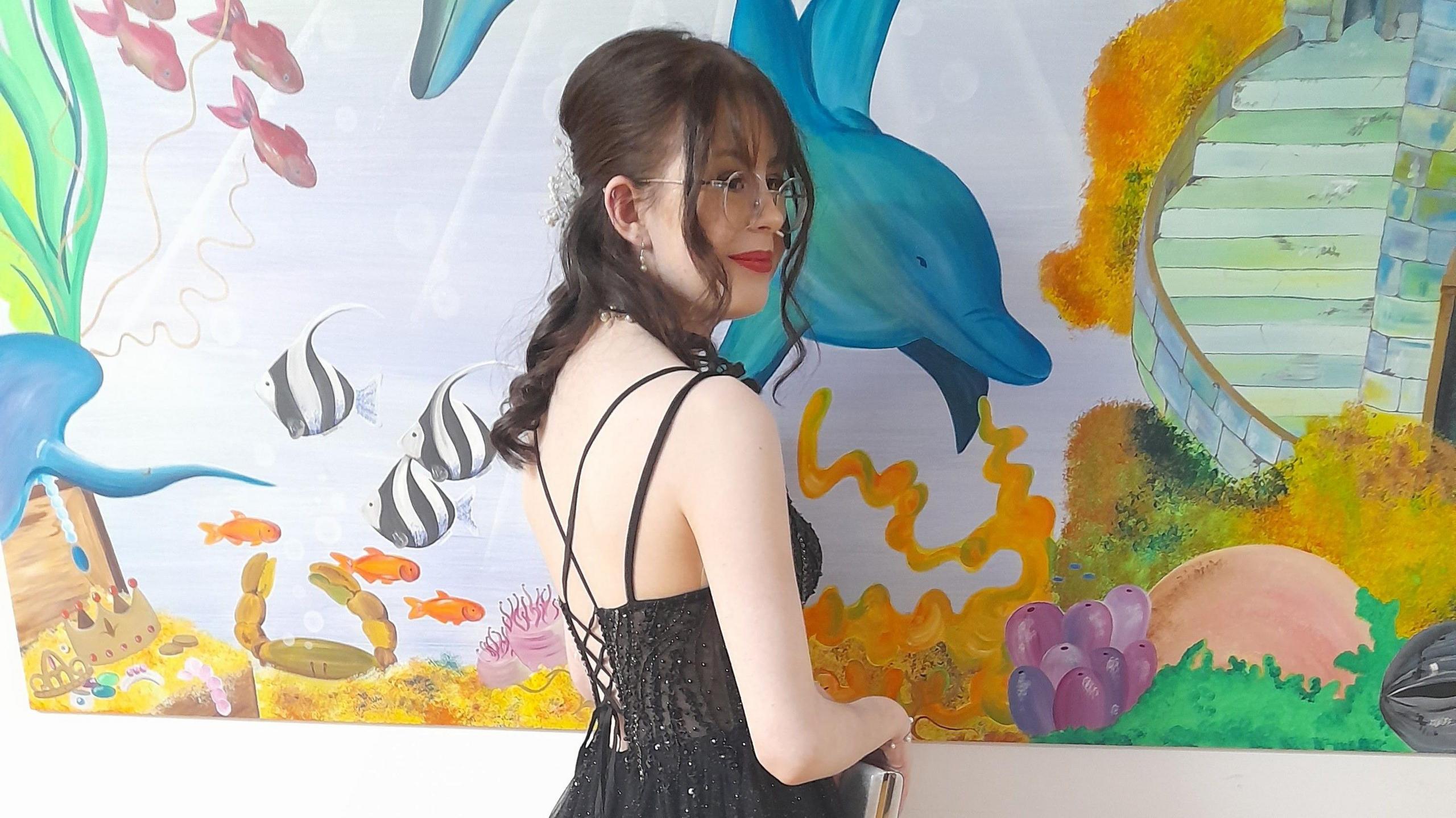 The back of Ellie, who is in a black prom dress, stood in front of a mural at Southampton Children's Hospital