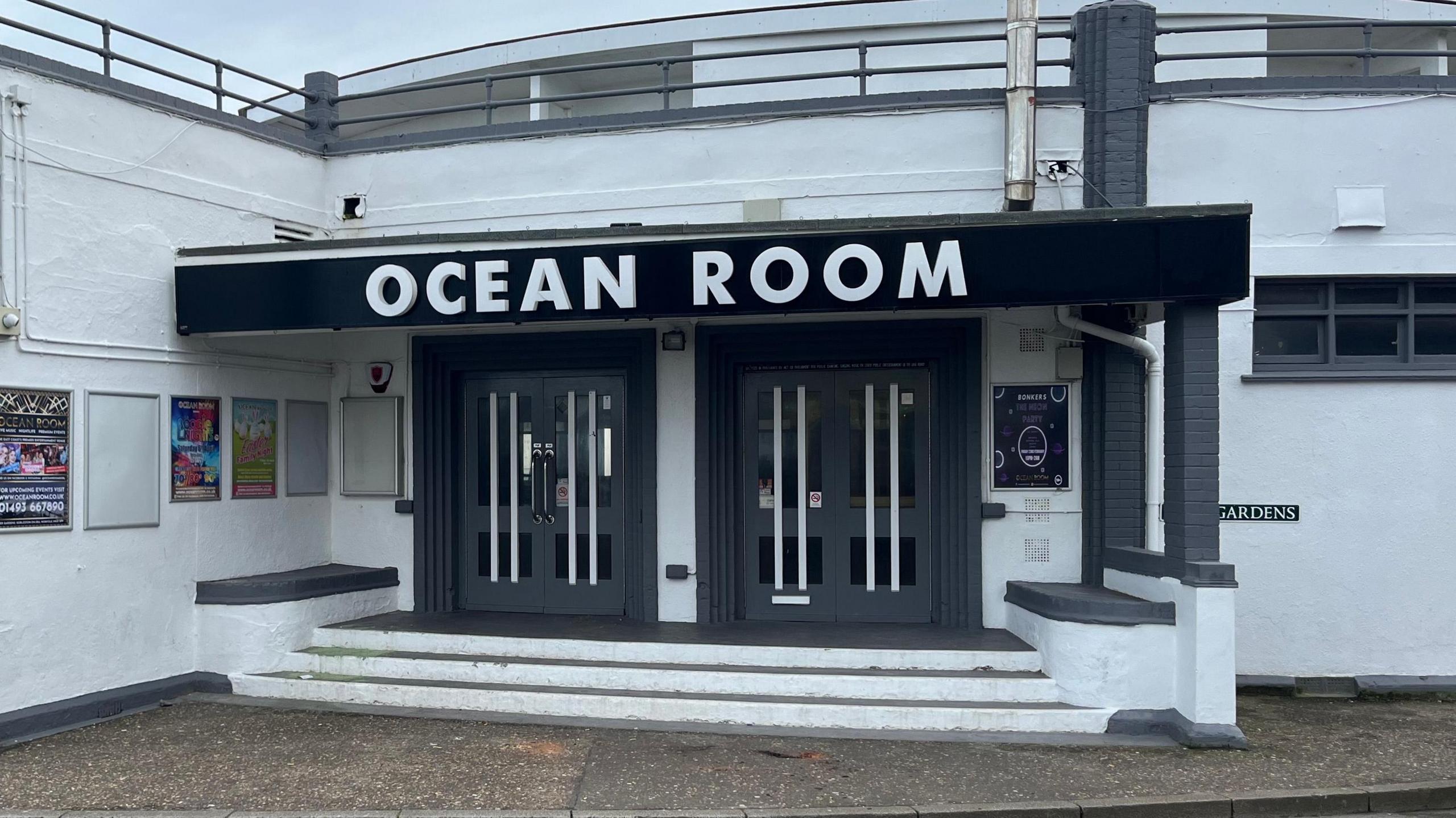 The outside of Ocean Room, a former dance venue in Gorleston, in Norfolk. The outside of the building is painted white with the doors painted grey. There is a sign on top of the building on a black background, which reads OCEAN ROOM, in white letters.