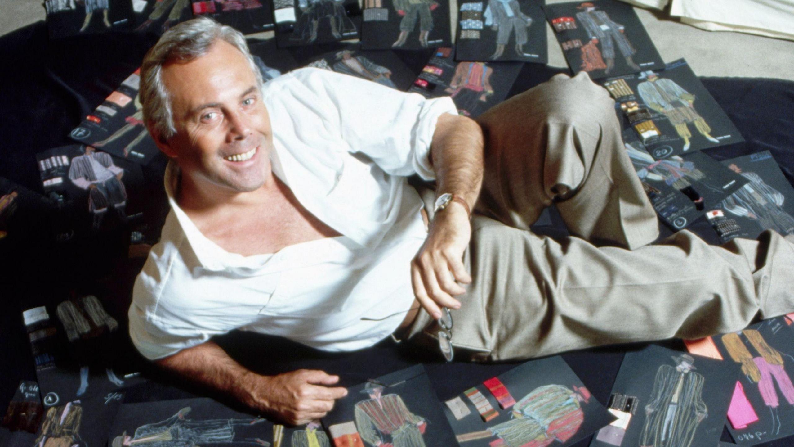 Giorgio Armani lying on dozens of black sheets showing clothes sketches on the floor, in 1982