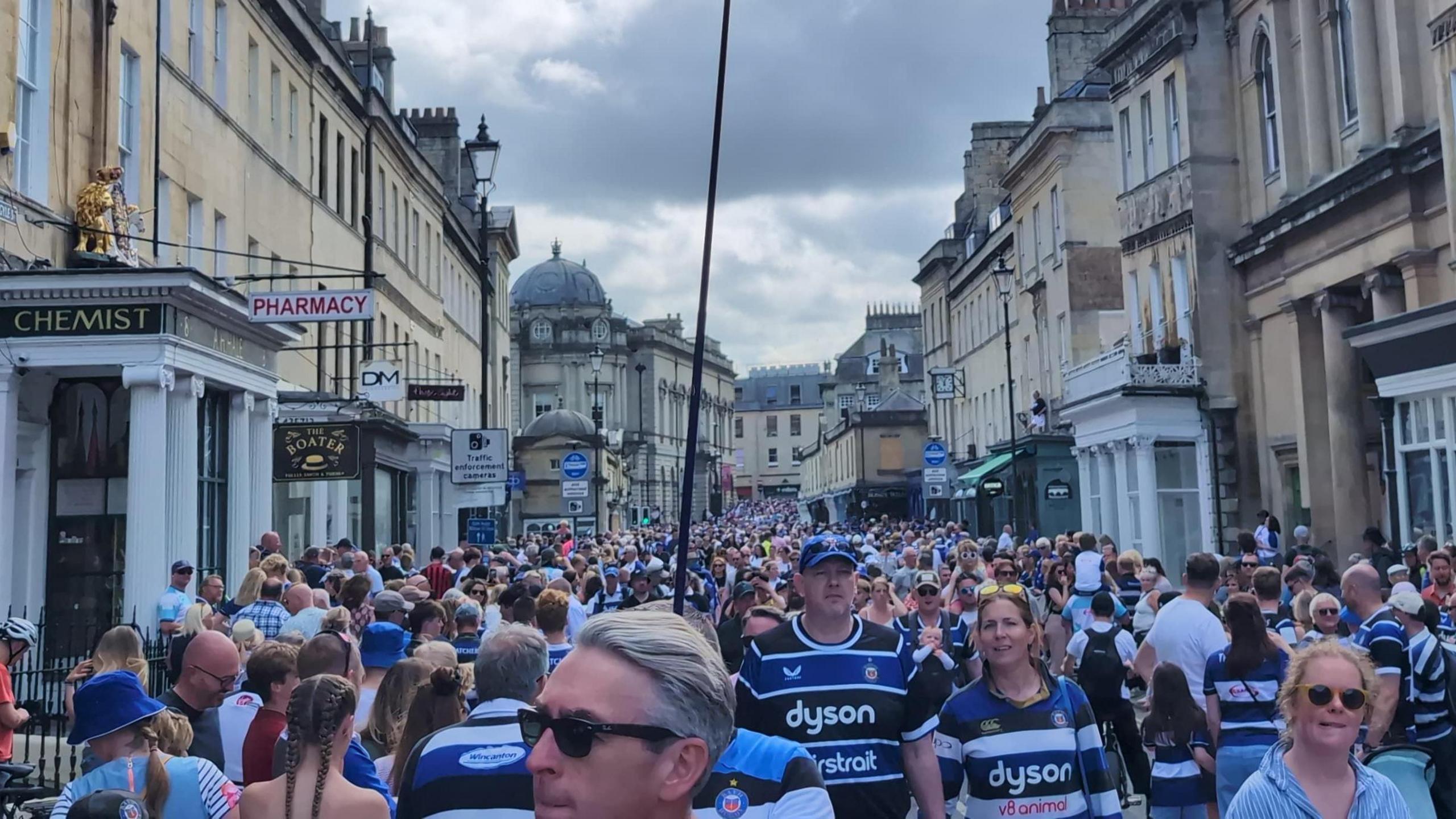 A full city centre street in Bath. Many are wearing Bath rugby shirts.