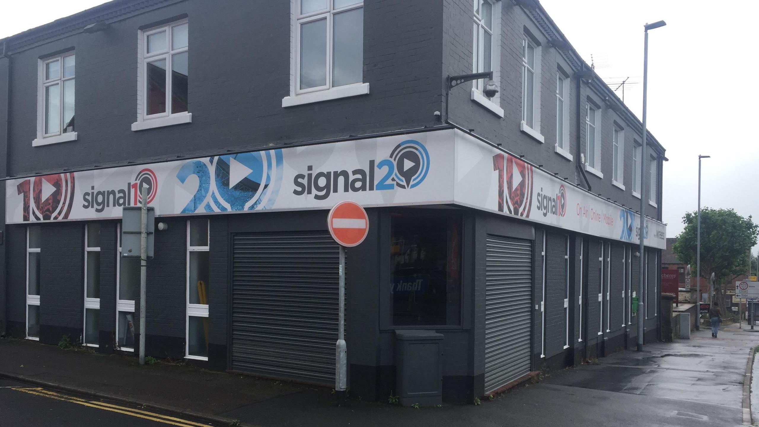 A grey two-storey building with shutters on the corners, and signs above branded Signal 1 and Signal 2