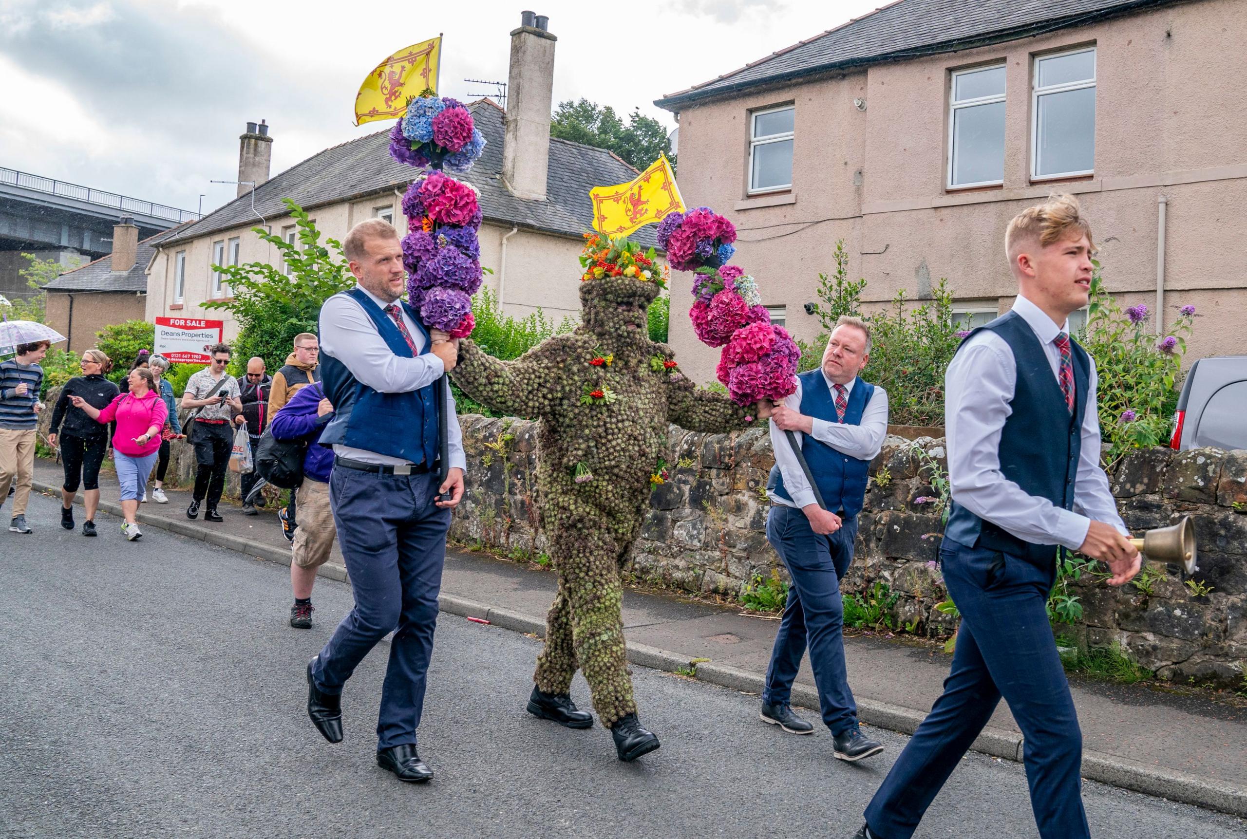 Burryman walking through the street with minders and supporters