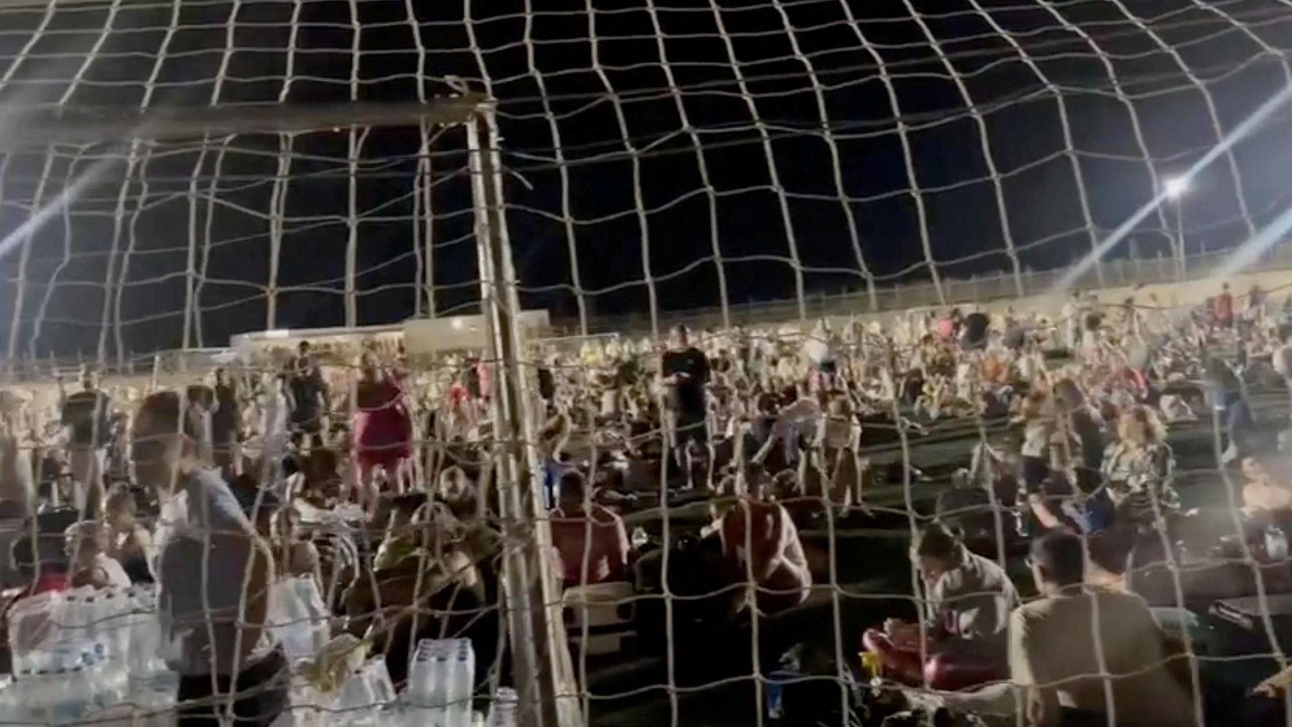 Evacuees sitting on a football field after wildfires in Kos